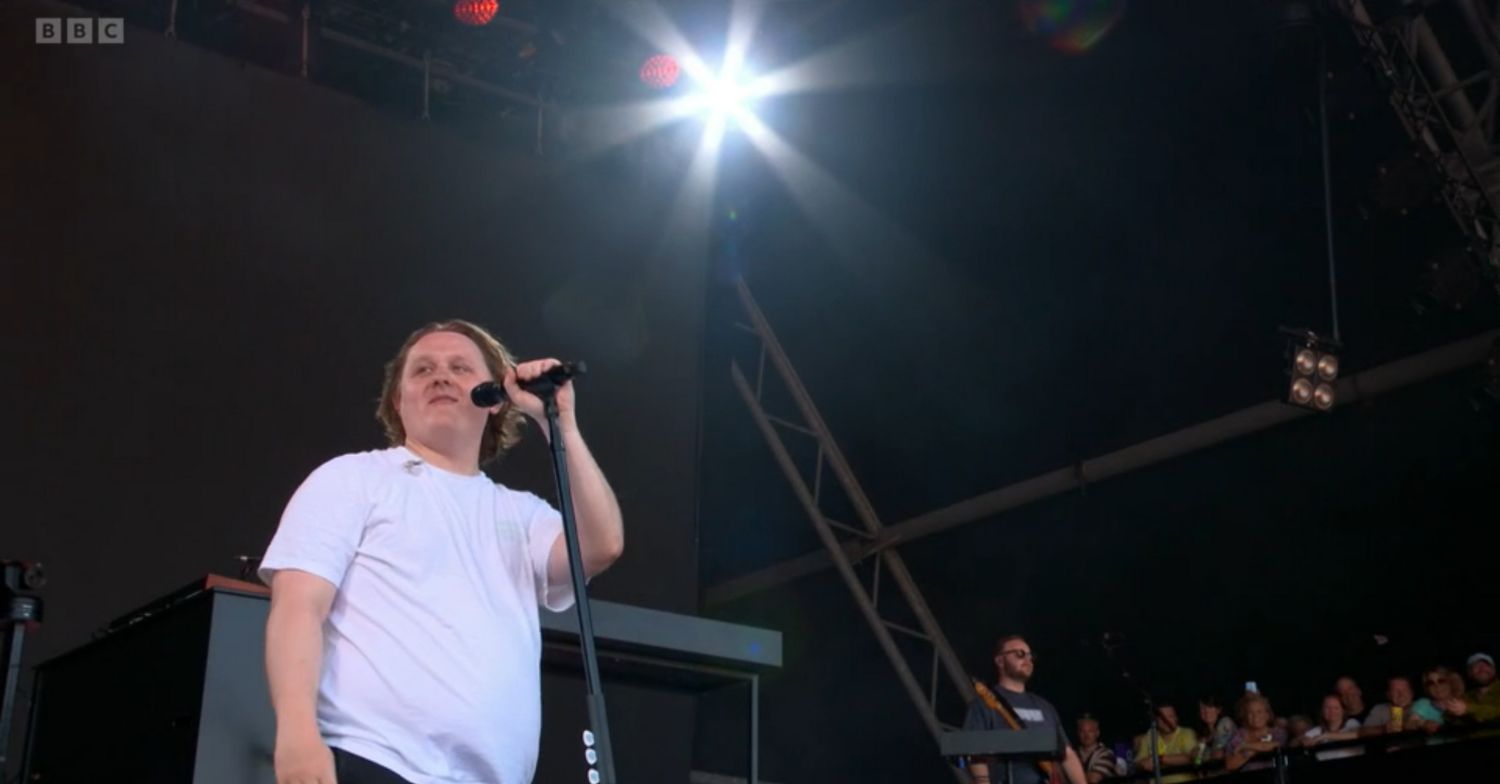 Singer Lewis Capaldi on stage performing at Glastonbury holding a microphone