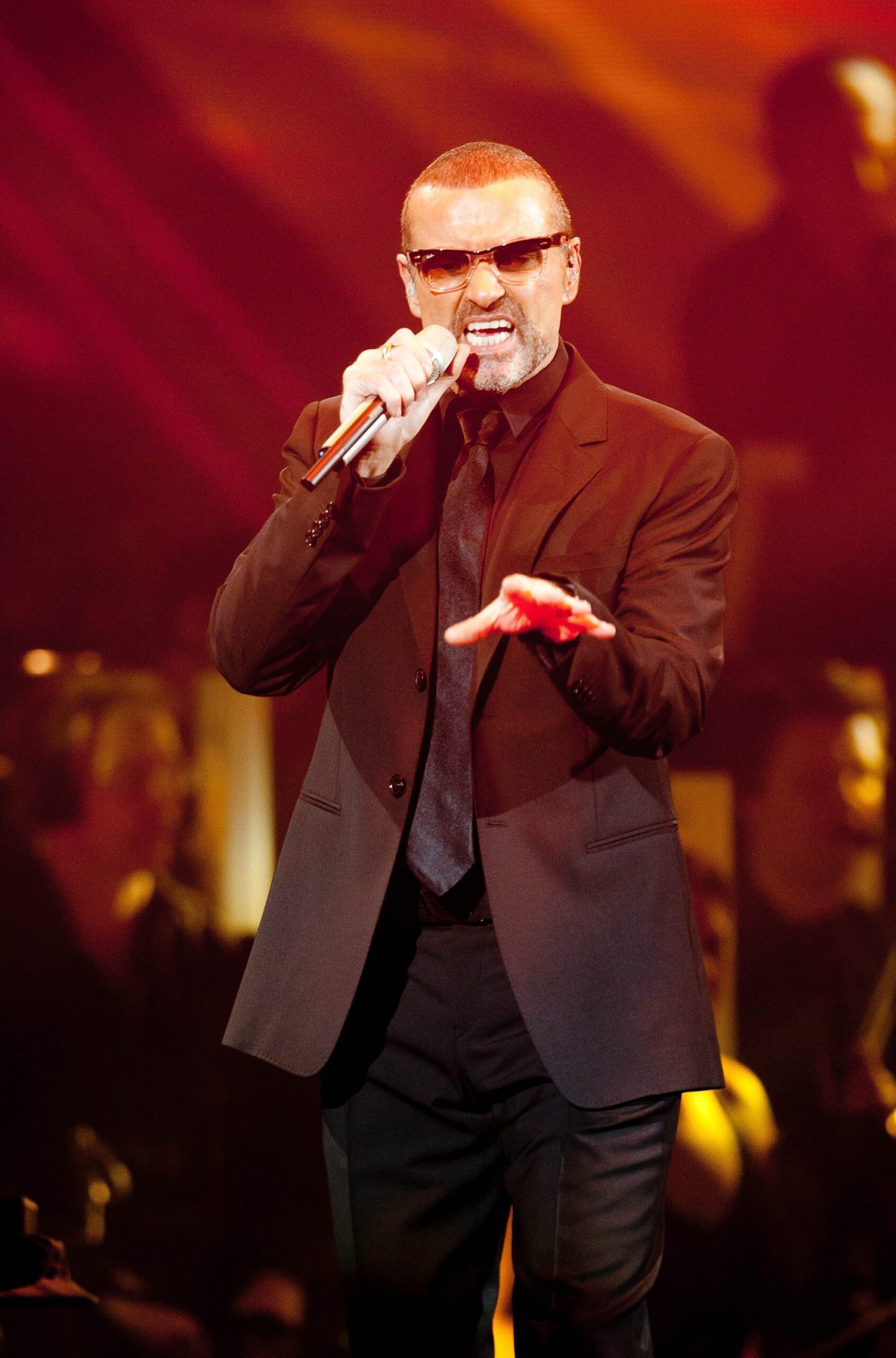 George Michael on stage singing against a red background