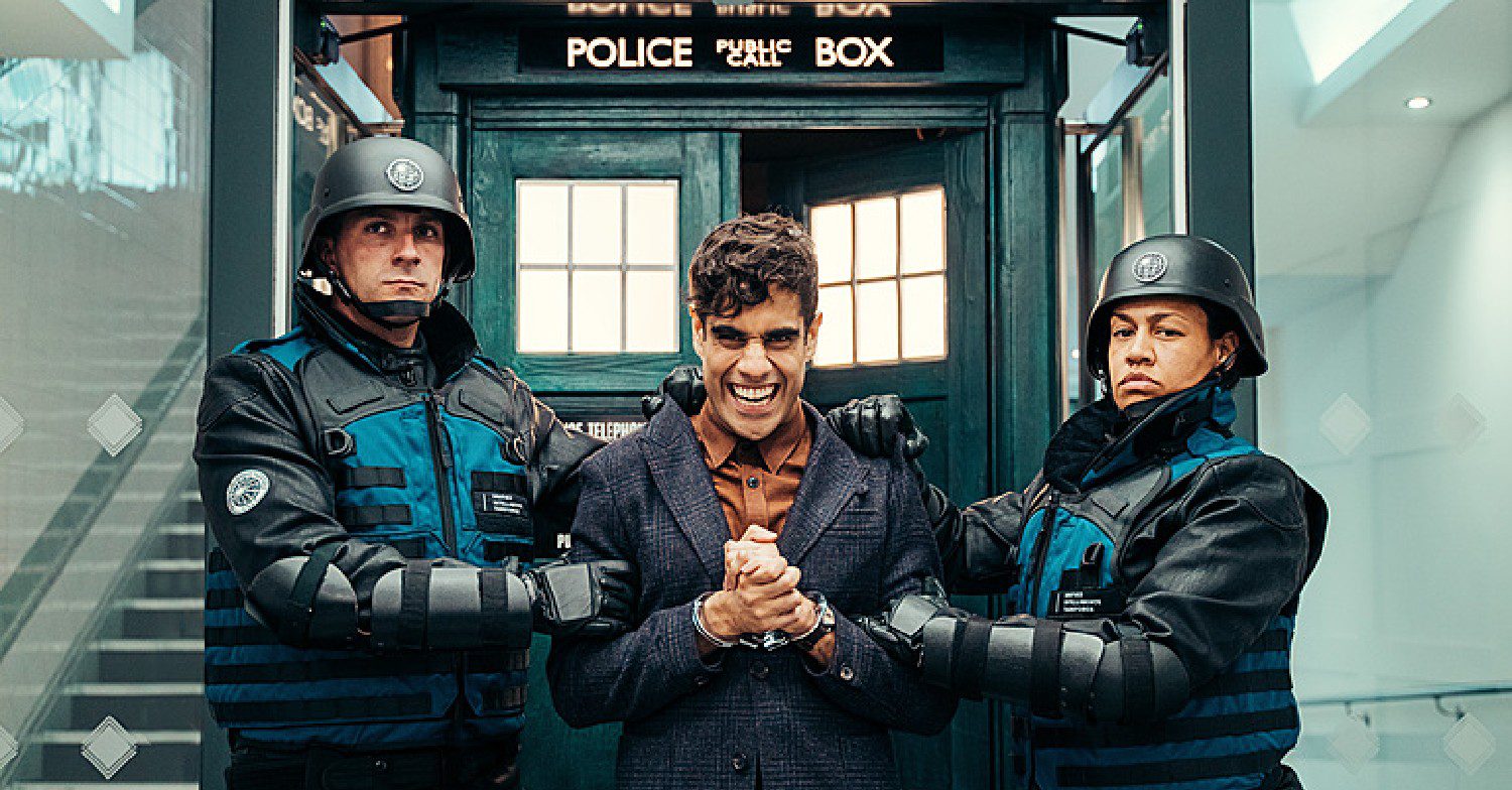 Actor Sacha Dhawan playing Villian The Master in Doctor Who. He is stood in handcuffs outside the Tardis
