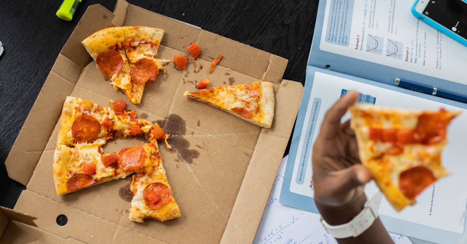 A person eats a slice of pizza from a takeaway delivery