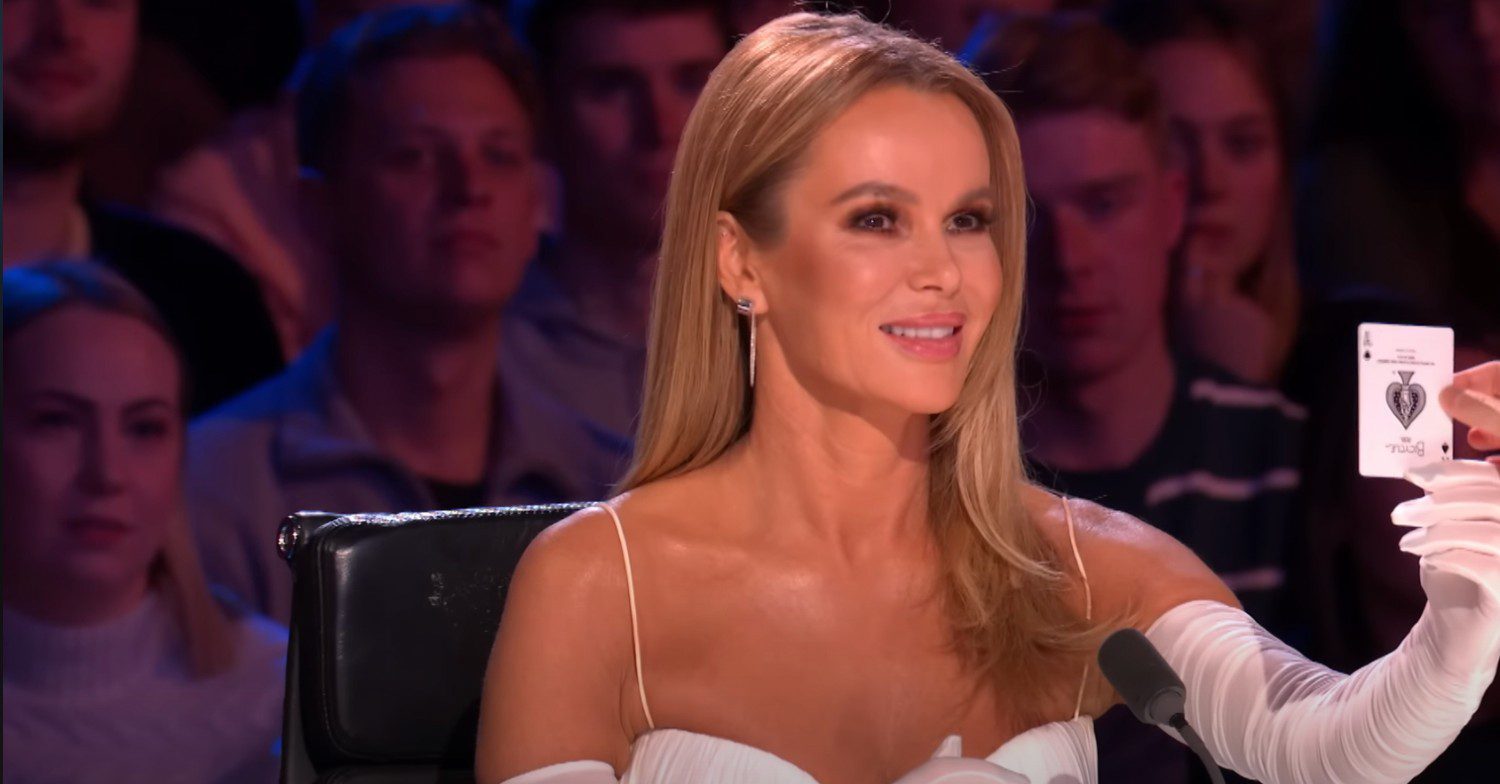 Amanda Holden wearing white as she holds the card of a magician while appearing on Britain's Got Talent