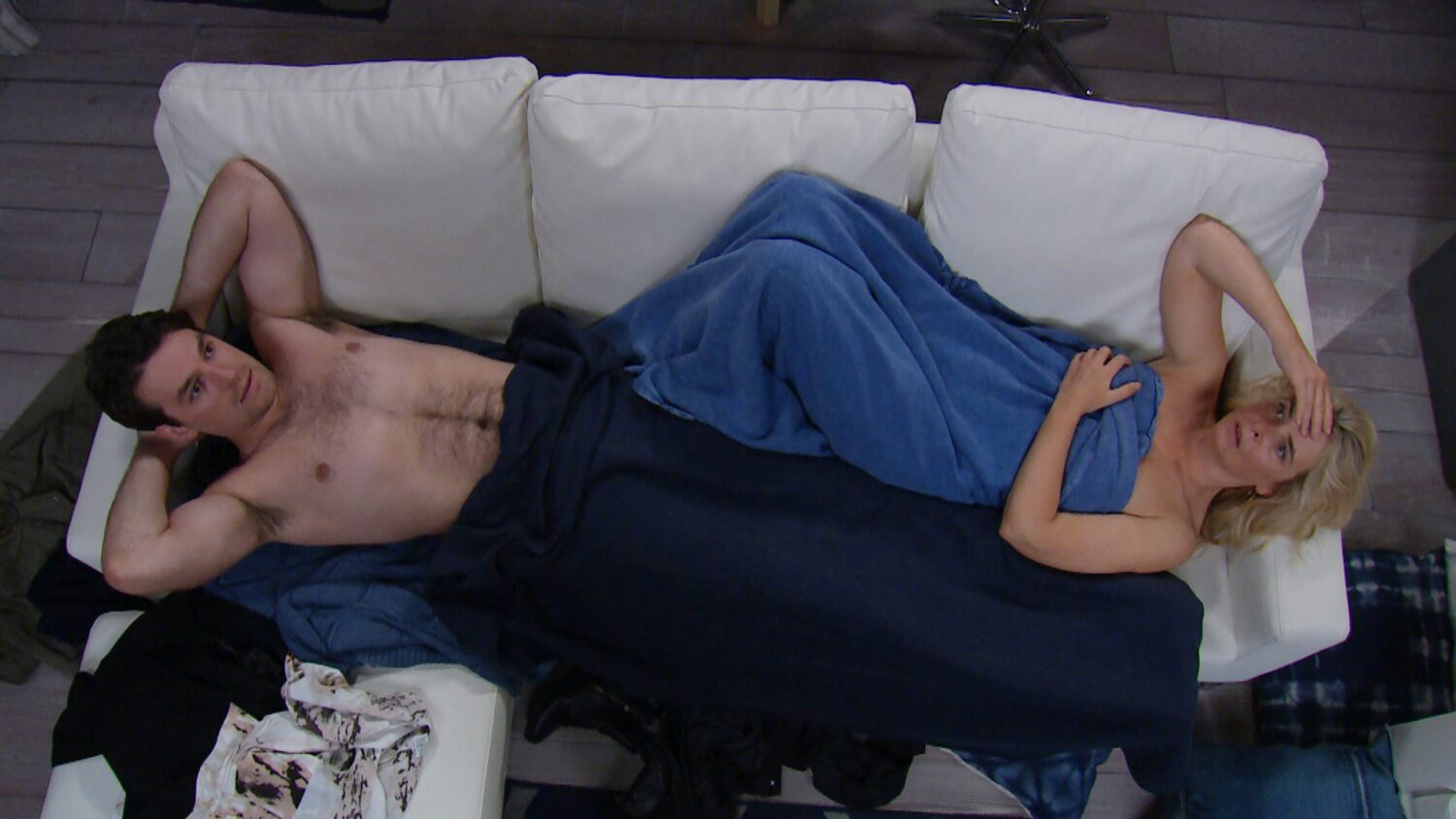 Mack and Charity lie on the sofa covered in blankets looking embarrassed after sleeping together