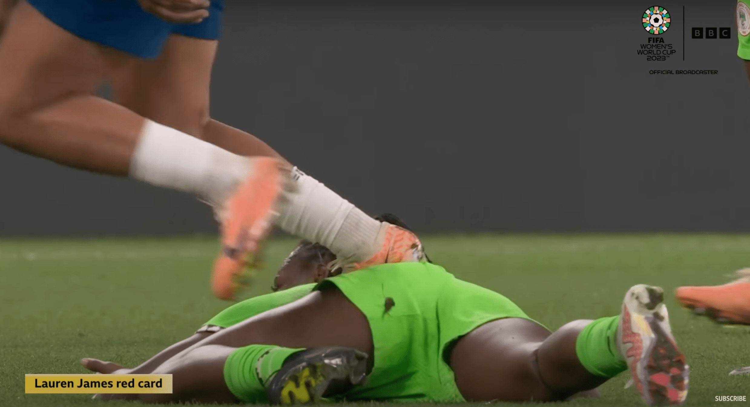 Footballer on floor in green with another player treading on her back