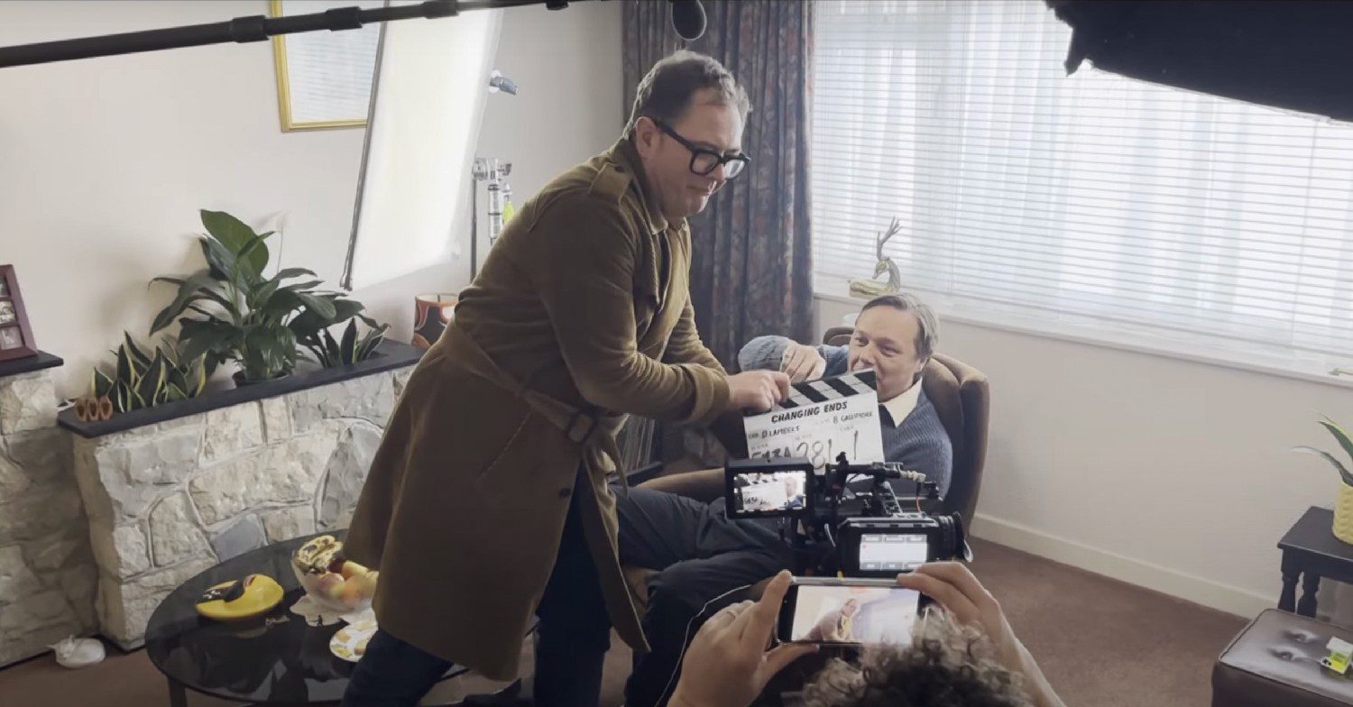 Comedian Alan Carr holding a clapper board on the set of the show Changing Ends