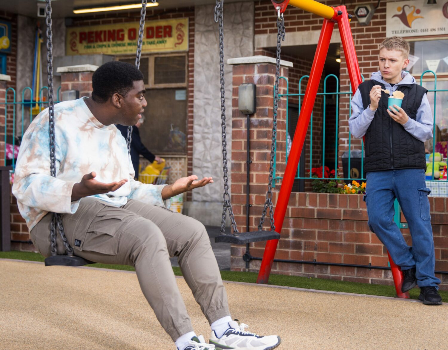 Gav in Coronation Street sits on the swing and laughs as Max has ice cream