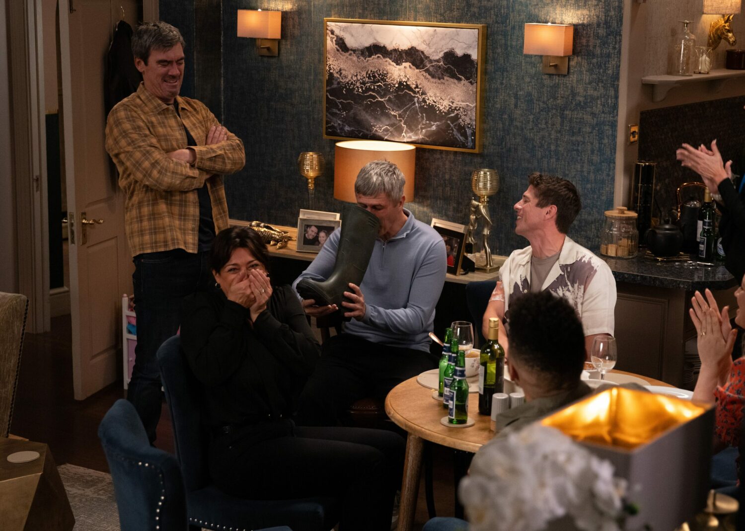 Emmerdale's Cain, Moira, Nicky and Nate are gathered around a table as they laugh at Caleb drinking from the Dingle welly in the back of the pub
