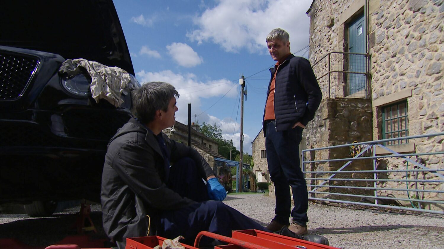 Emmerdale's Cain and Caleb are talking to each other outside as Cain works on a car