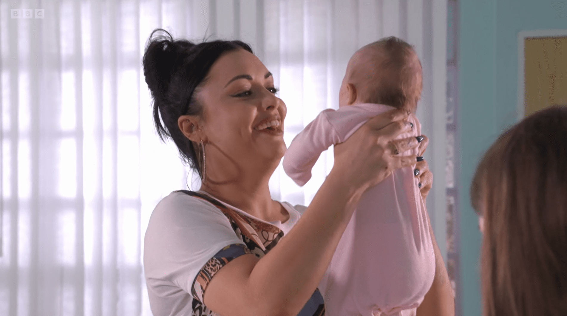 Whitney in EastEnders holds baby Charli up and smiles 