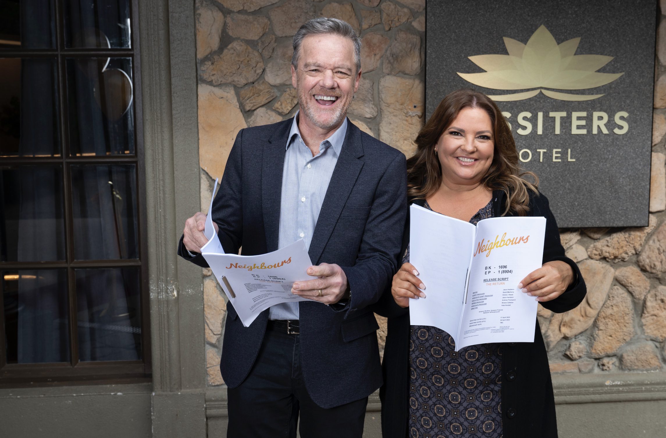 Paul and Terese from Neighbours smile and hold scripts outside Lassiters