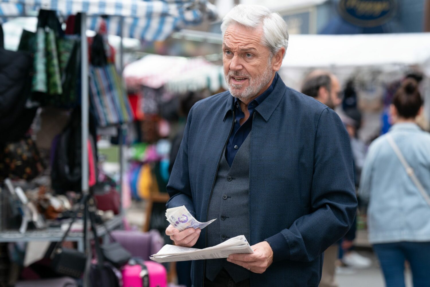 Rocky in EastEnders holds money and looks frustrated