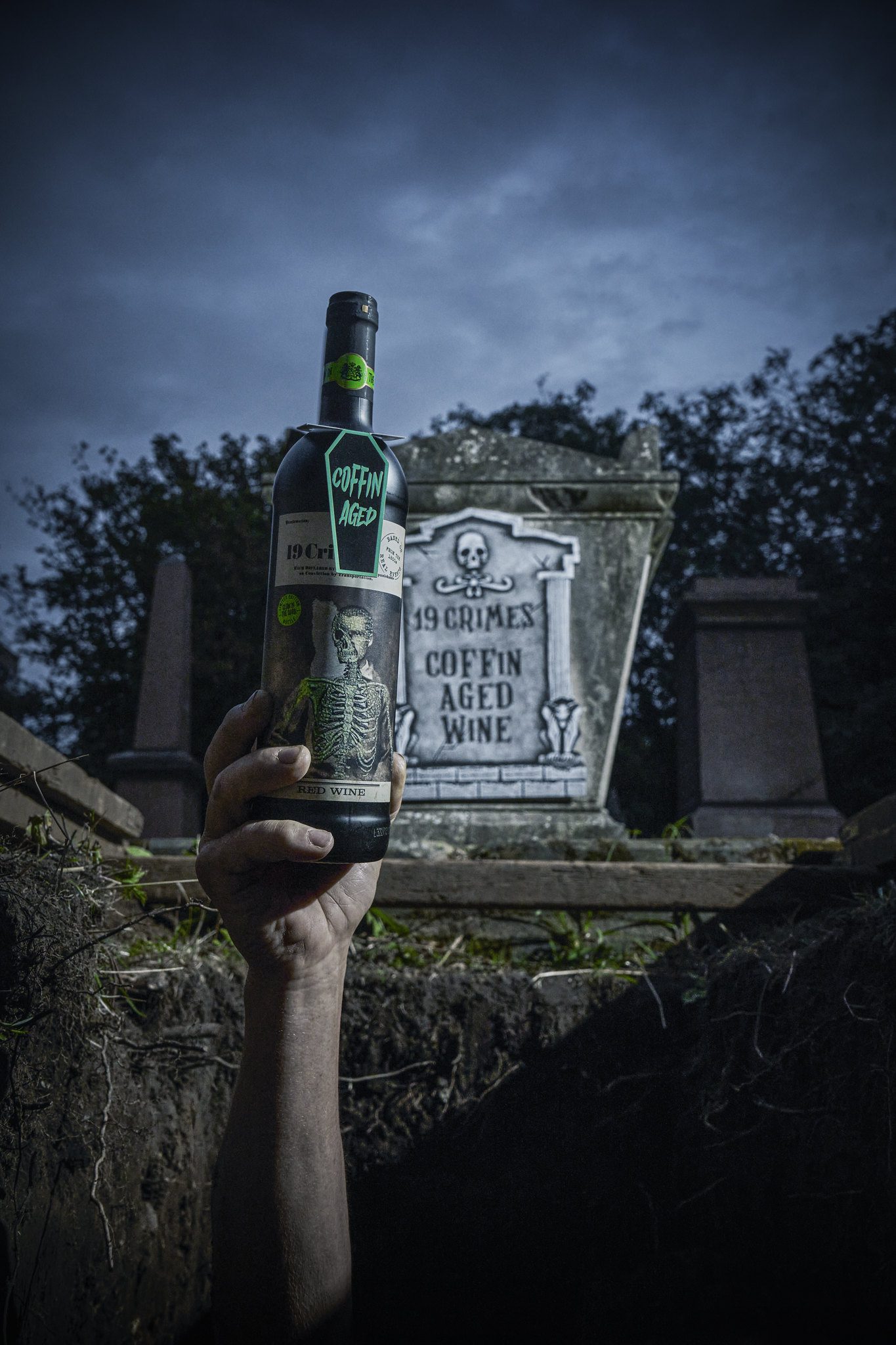 Hand holding 19 Crimes wine bottle out of a grave
