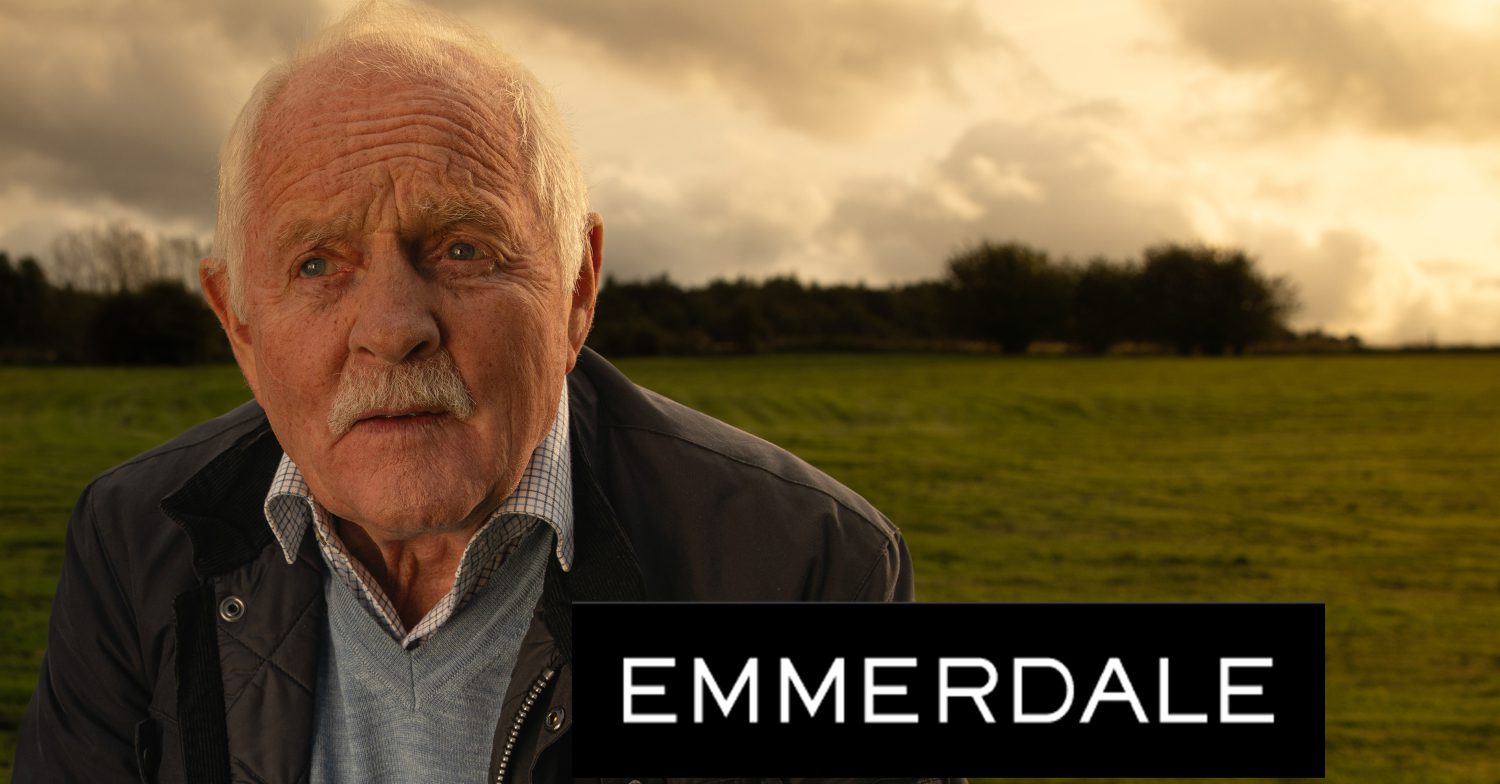 Emmerdale's Eric is looking sad in a field, the Emmerdale logo