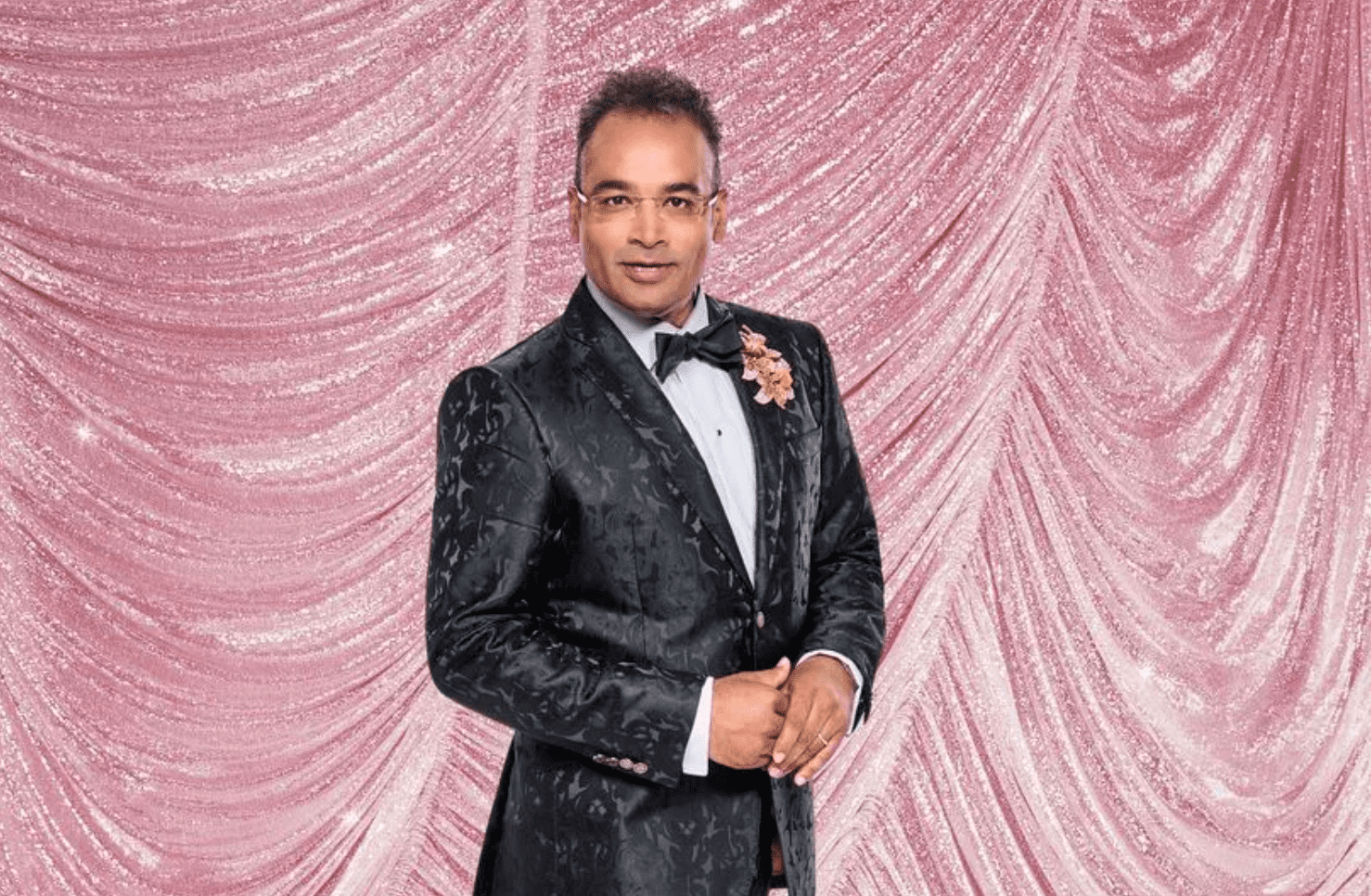 Krishnan Guru-Murthy smiling on shimmery pink Strictly background
