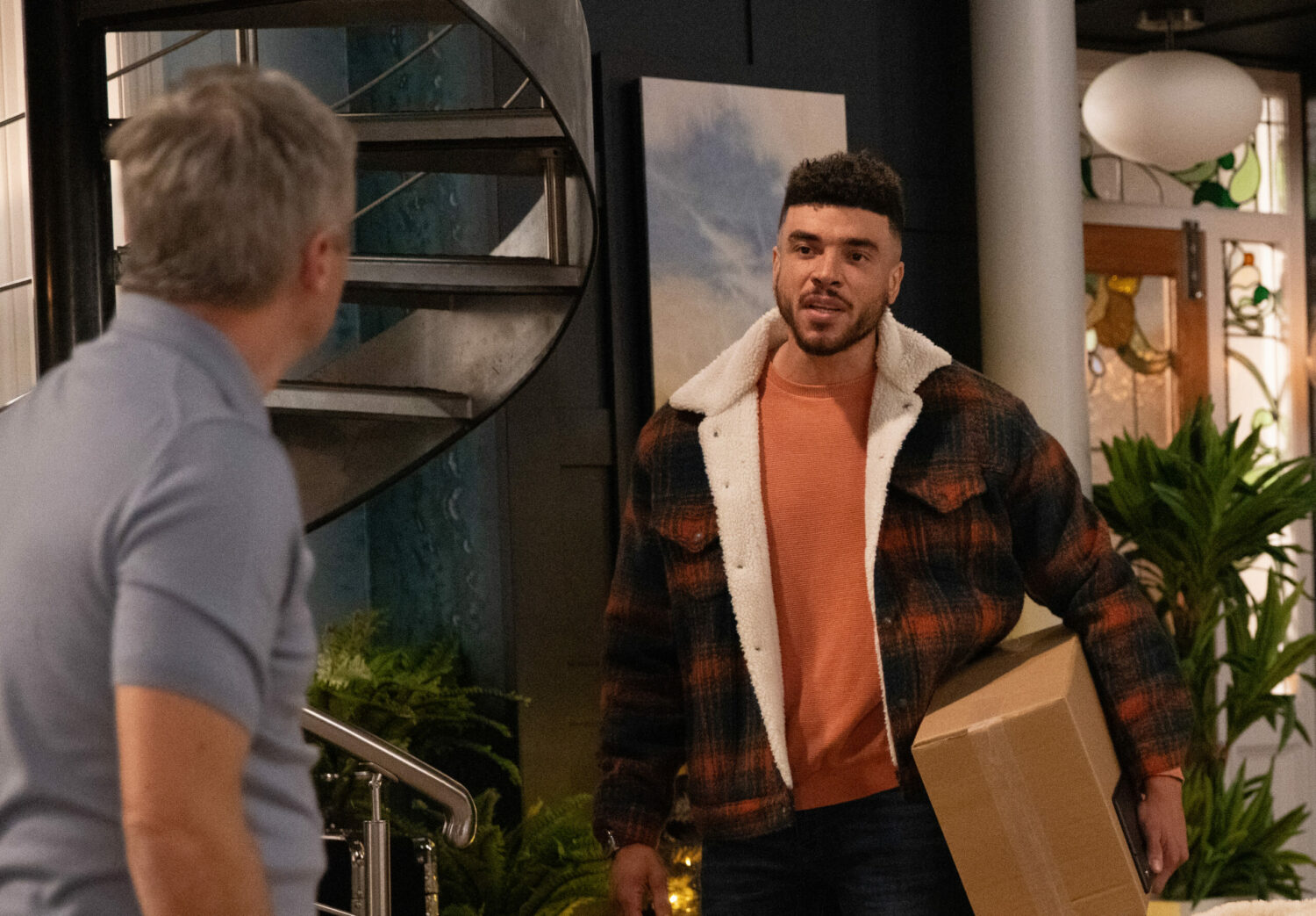 Nate confronts Caleb and Tracy, holding a package under his arm on Emmerdale