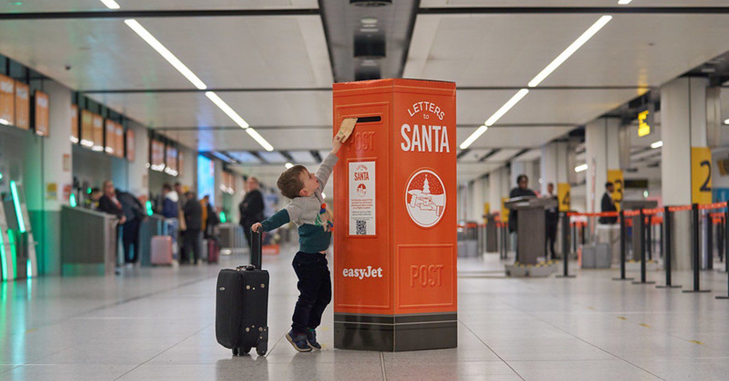 Kid putting a letter in an orange postbox in the airport 