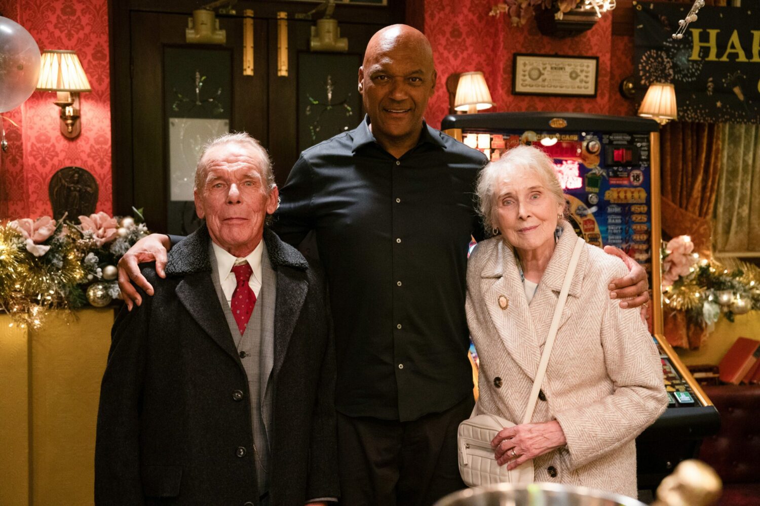 George stands smiling with his parents on EastEnders
