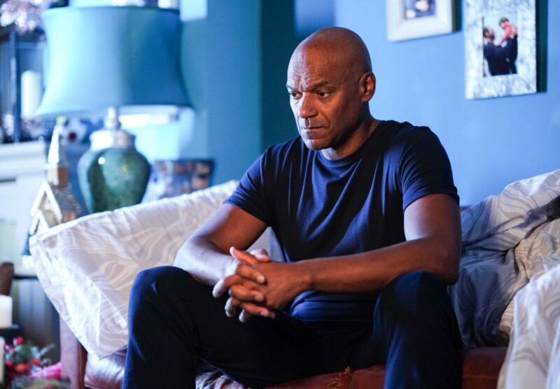George looks worried as he sits on the sofa on EastEnders