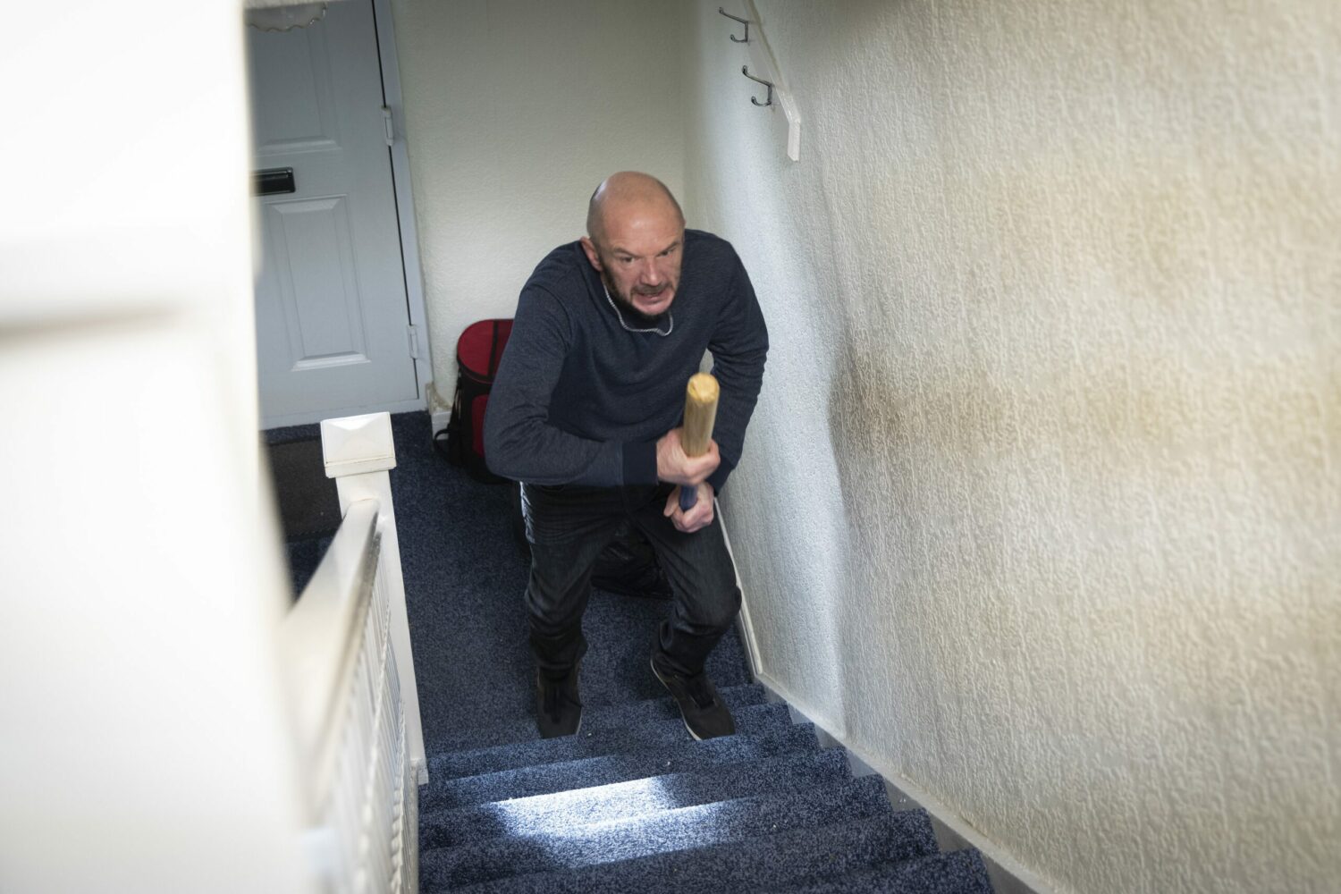 Terry running up stairs with baseball bat on Corrie