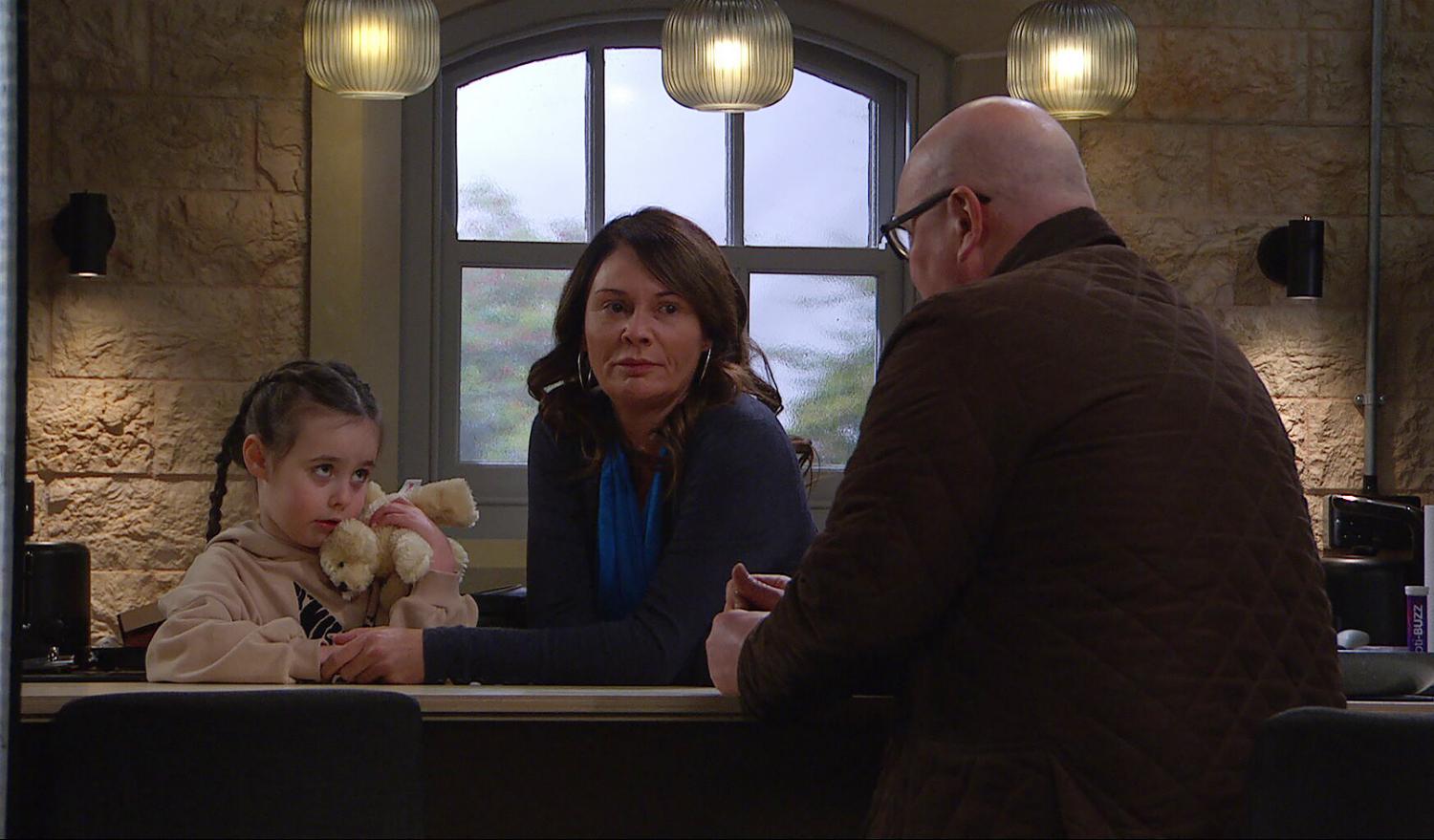 Eve in Emmerdale cuddles her teddy as Chas holds her hand and looks sadly at Paddy