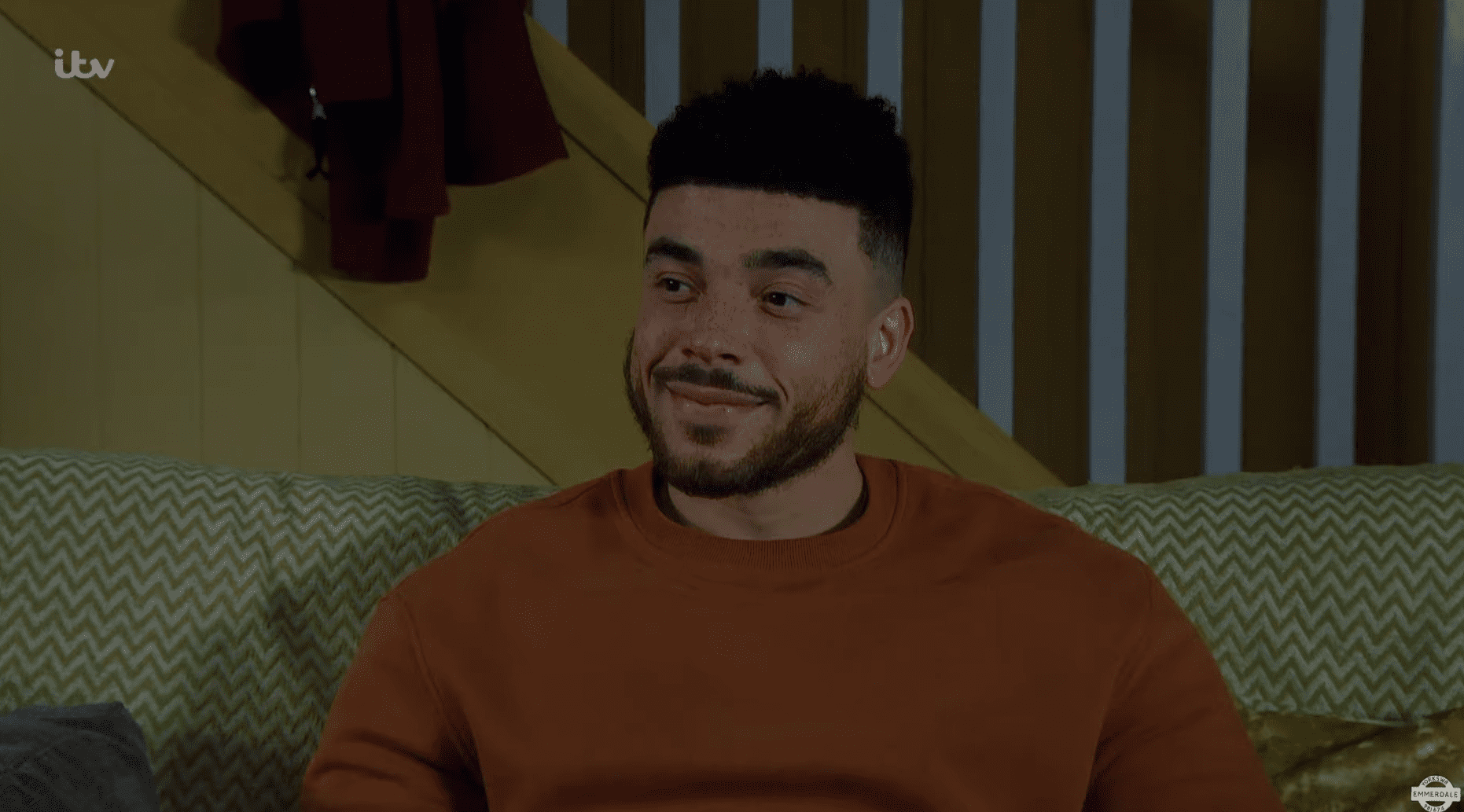 Emmerdale's Nate smiles as he sits on the sofa