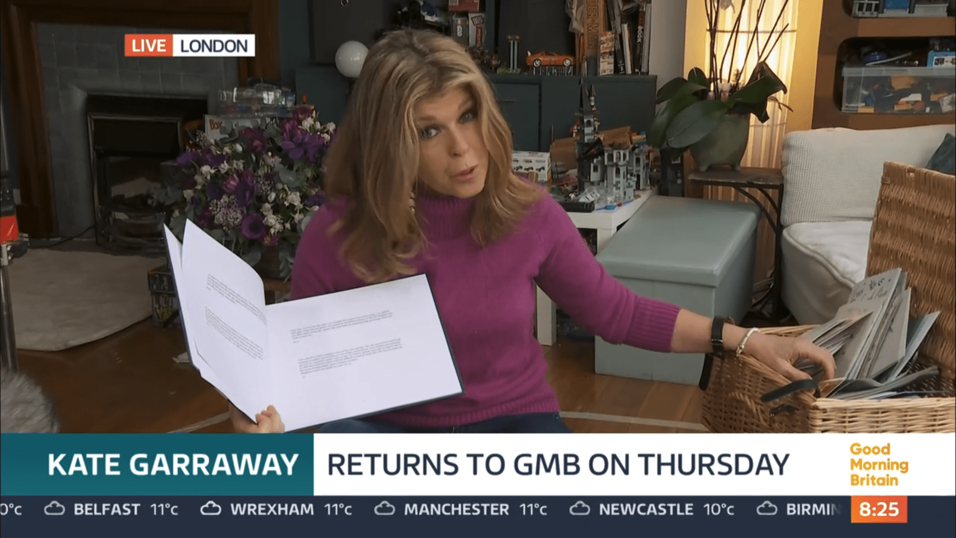 Kate Garraway in her home with a box of cards holding a book