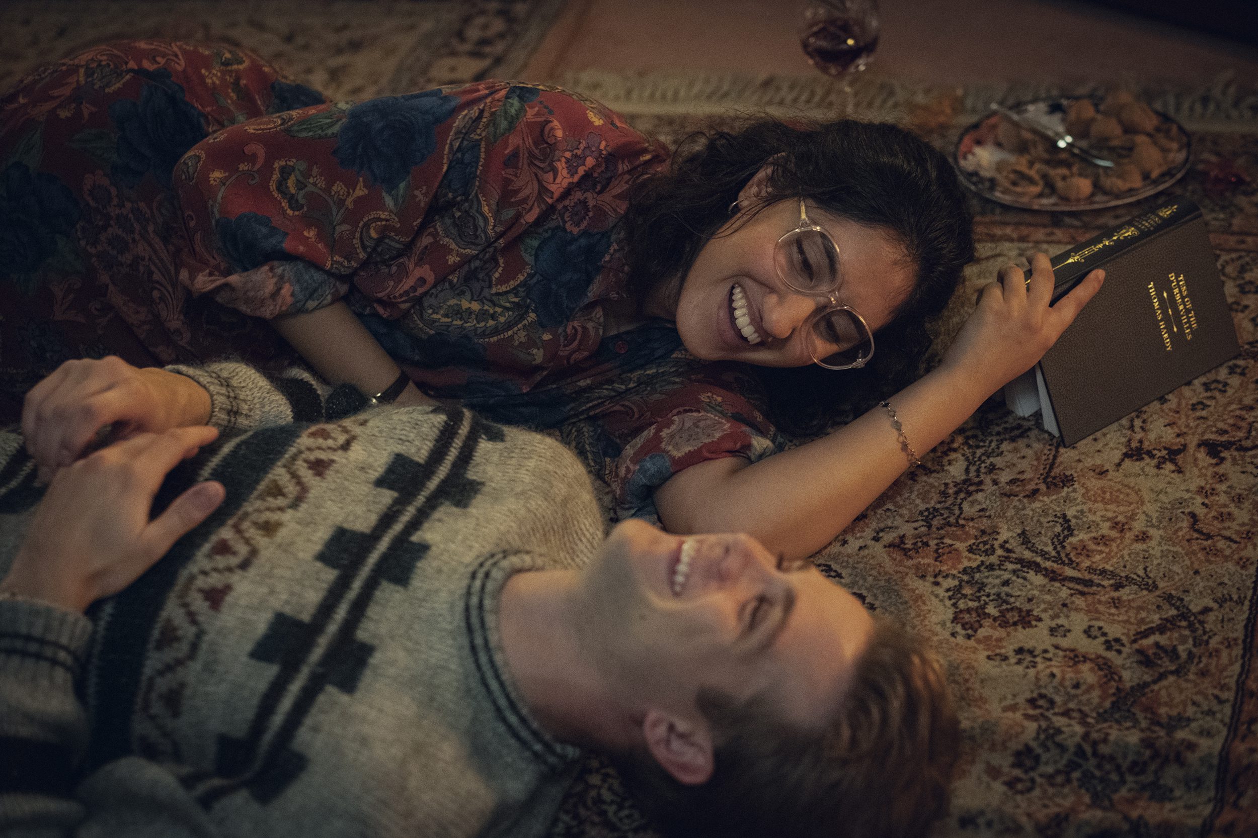 Ambika Mod and Leo Woodall in character as One Day's Emma and Dexter, laughing together on the floor