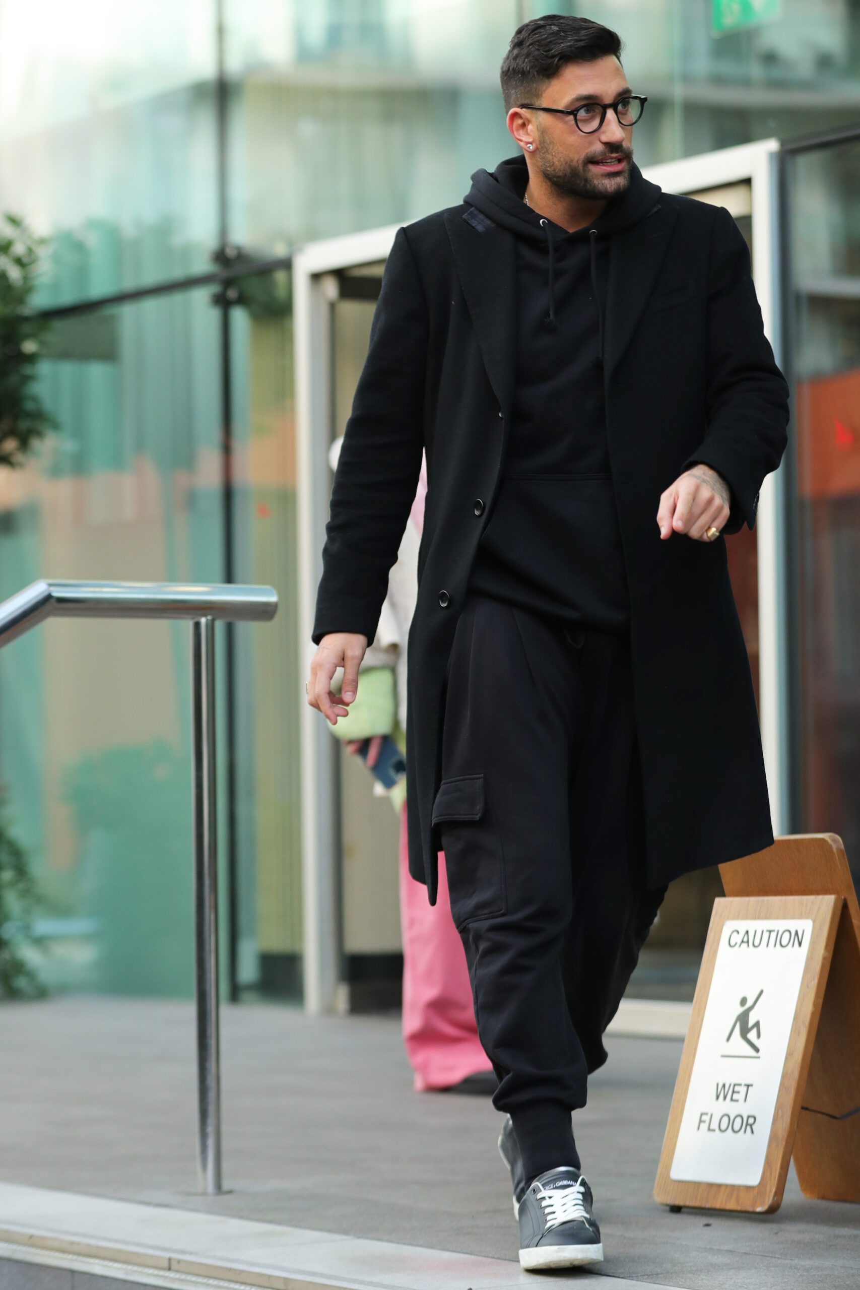 Giovanni Pernice wearing glasses and a black coat in the street