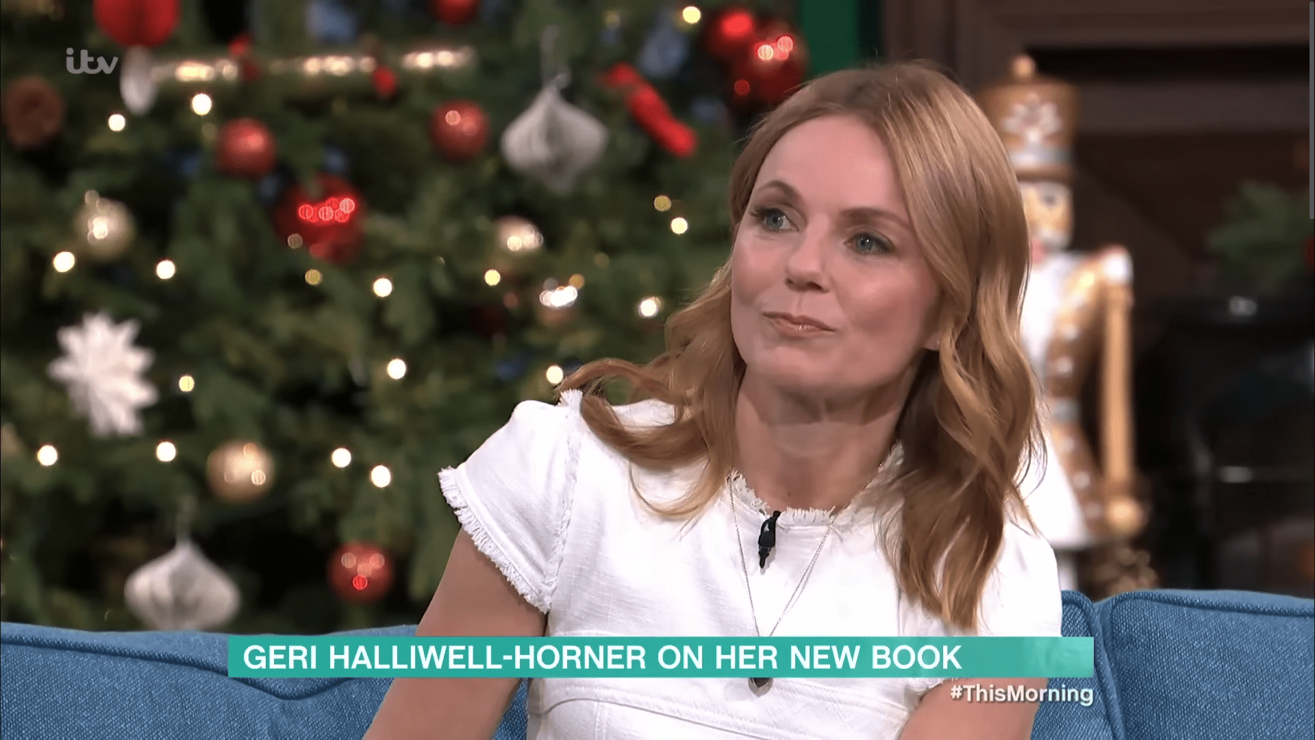 Geri Halliwell in a white top sitting in front of a Christmas tree
