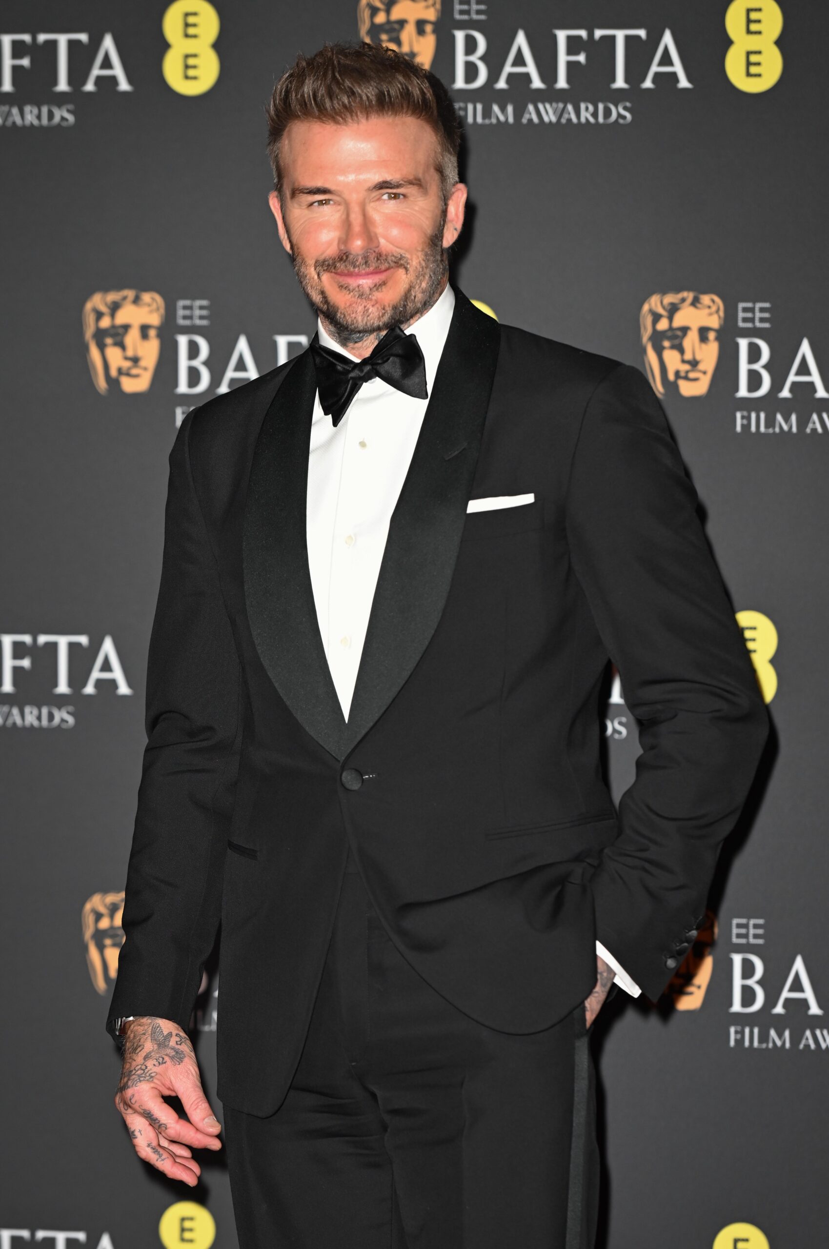 David Beckham smiling in a tuxedo on the BAFTAs red carpet