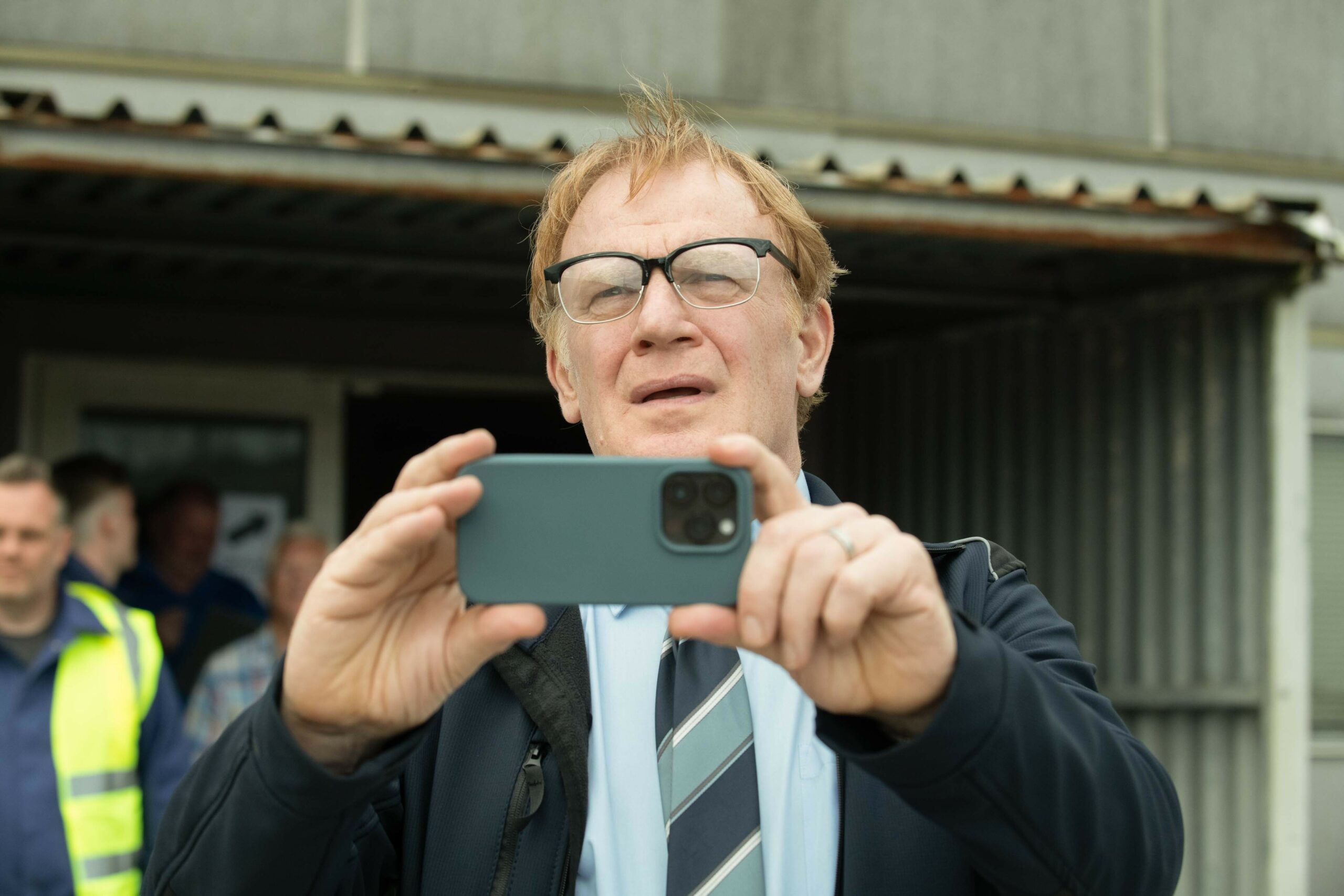 Mark Lewis Jones as Glynn, taking a photo on a camera phone, in The Way
