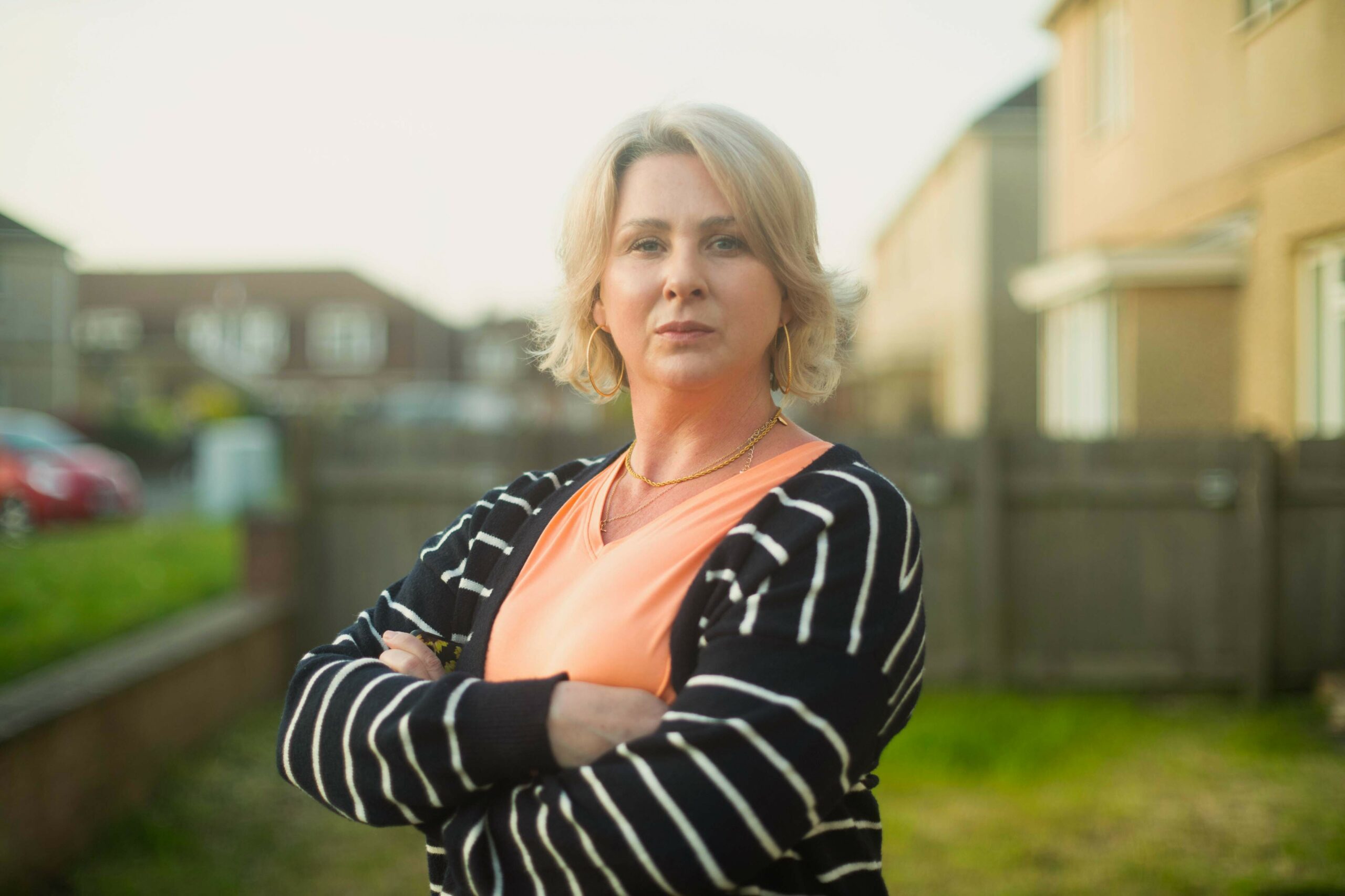 Mali Harries as Dee in The Way cast, wearing a stripy jumper with crossed arms