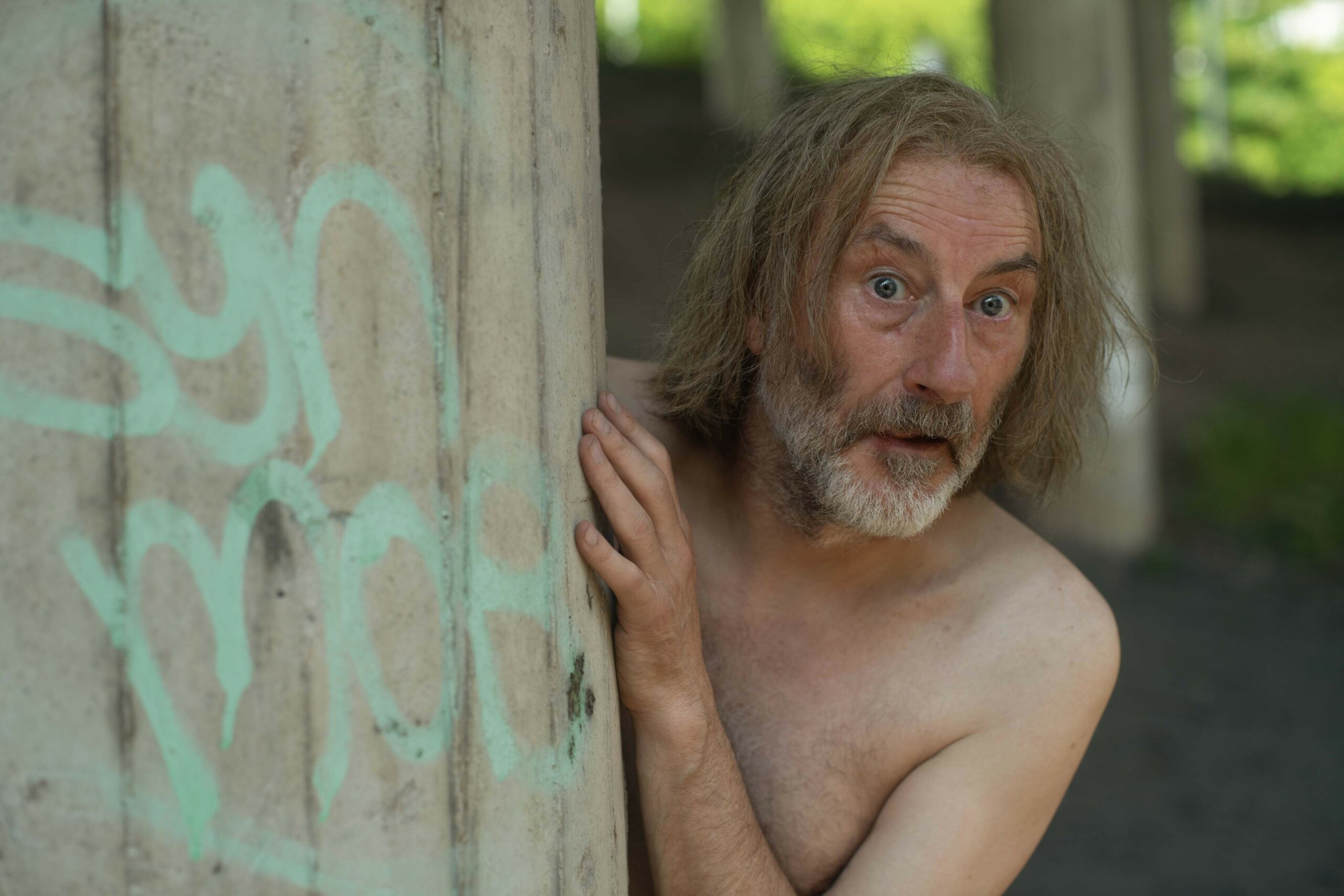 Jonathan Nefydd, playing The Prophet/Simon in the Way, glances behind a wall while shirtless