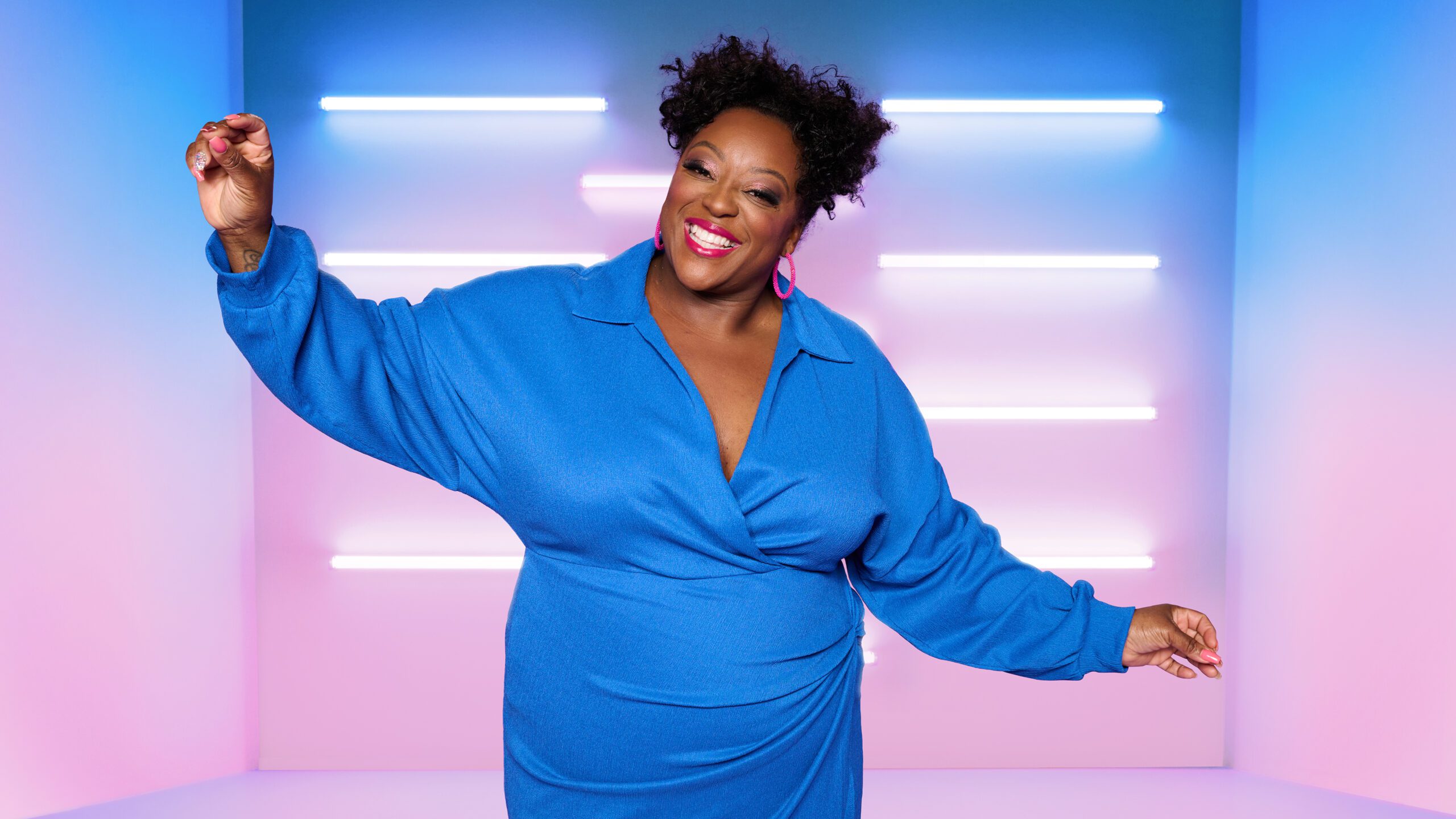 Loose Women star Judi Love wearing a blue shirt in front of a blue to pink gradient background