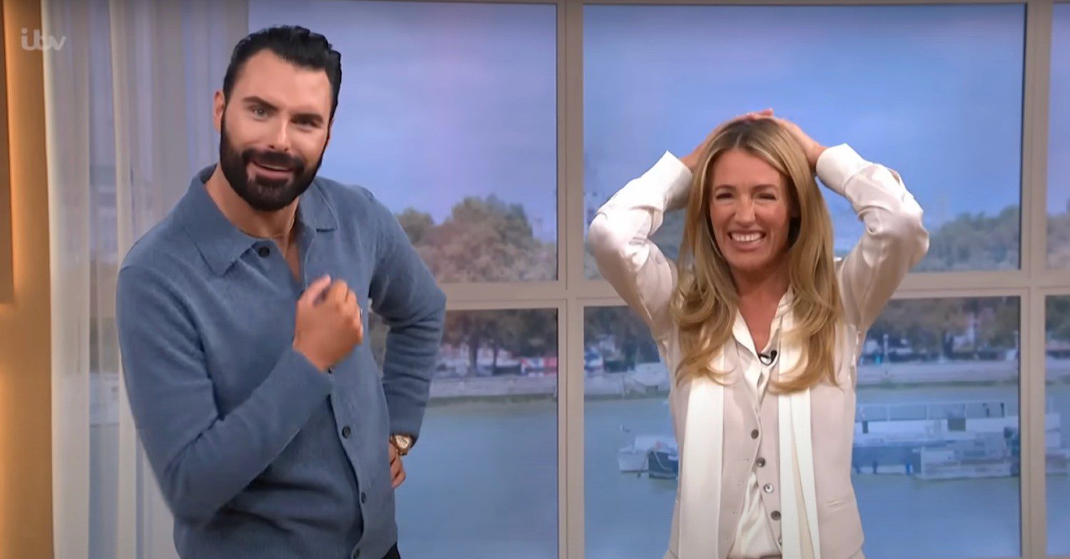 Cat Deeley wearing a white top with arms above her head pulling a frustrated expression with a smiling Rylan Clark in a blue shirt on This Morning