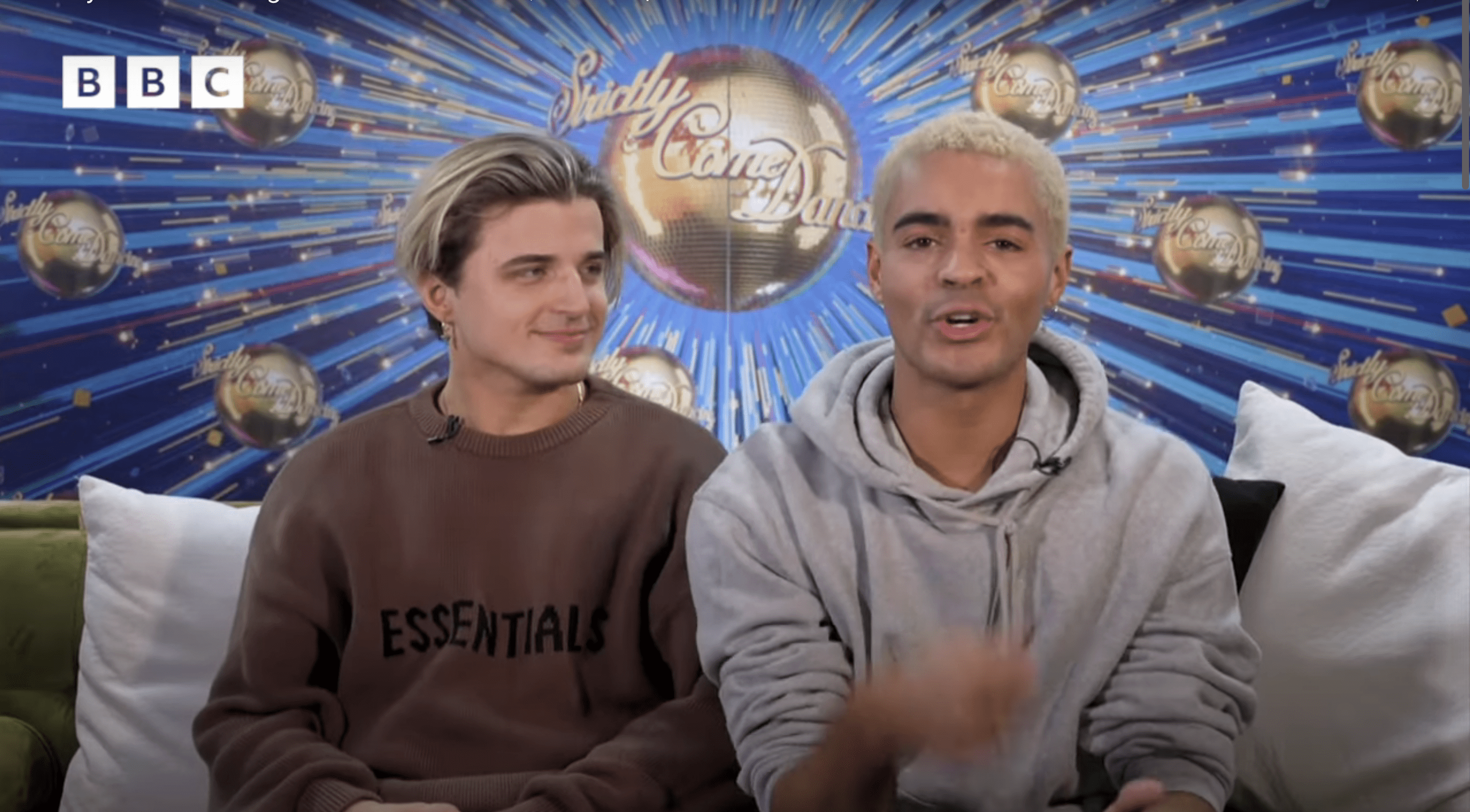 Nikita Kuzmin and Layton Williams sat against Strictly logo background on set of Newsround