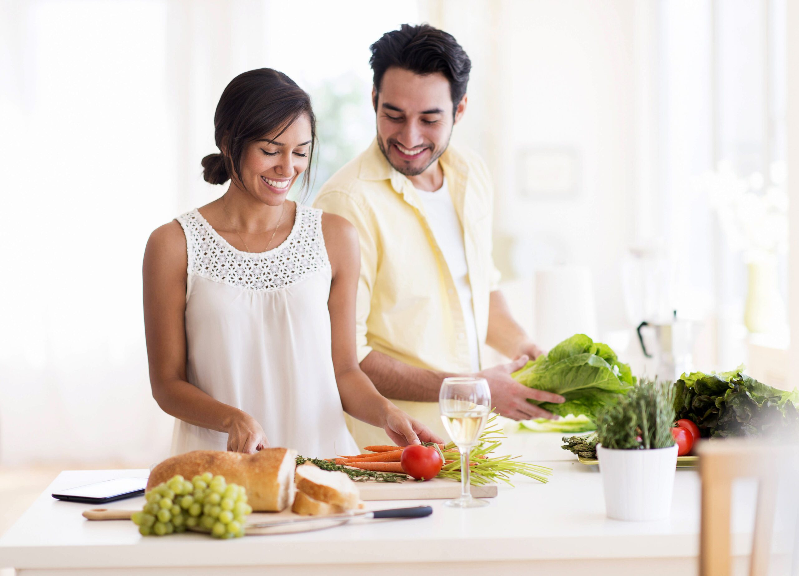 A woman and a man smiling in a sunny room preparing food