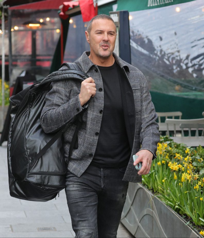 Paddy McGuinness smiles as he walks down the street carrying a large bag