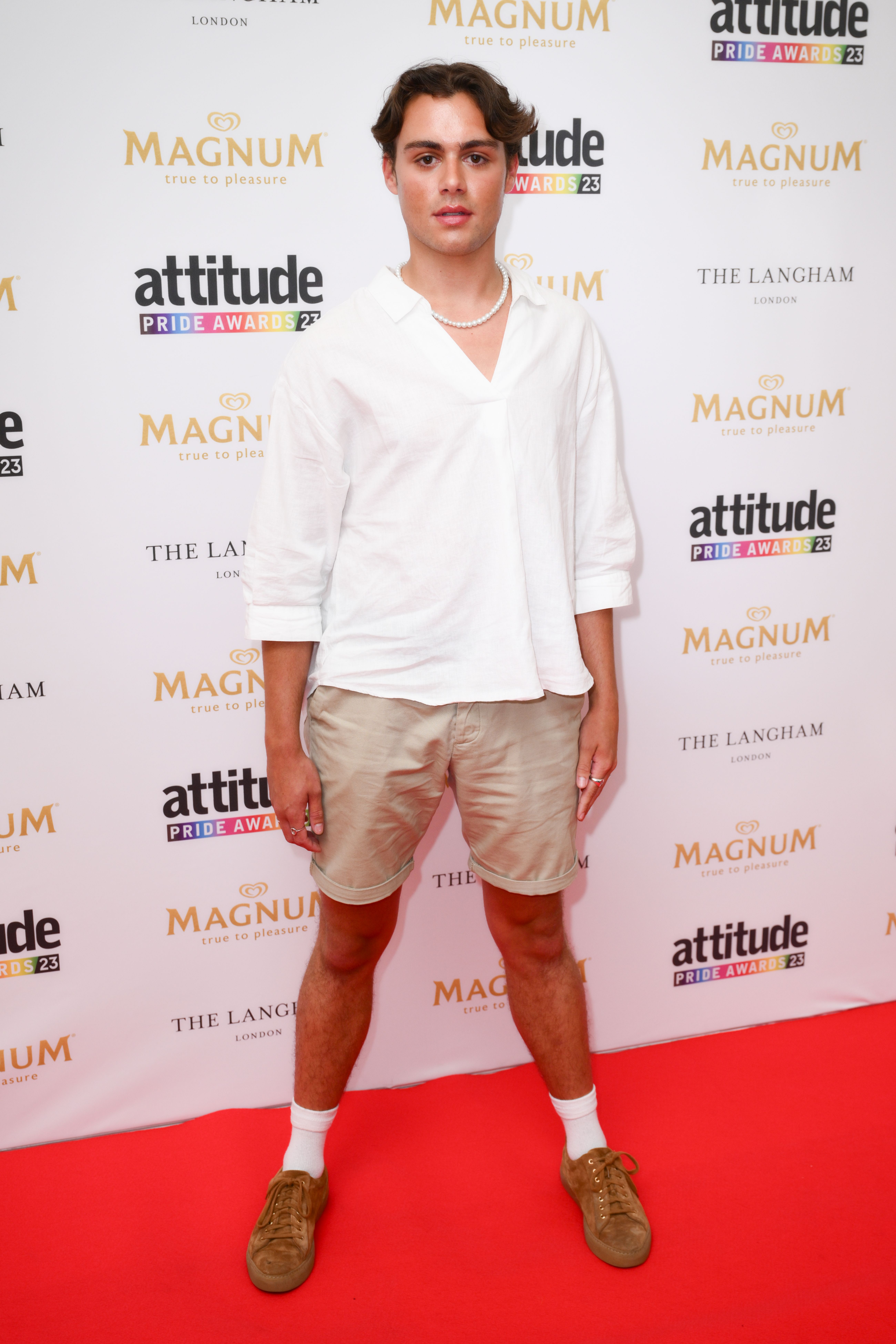 Bradley Riches wearing a white shirt and beige shorts to the Attitude Pride Awards red carpet