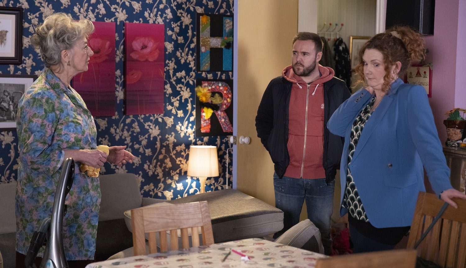 Evelyn in Corrie looks surprised and Tyrone looks annoyed while Fiz looks awkward.