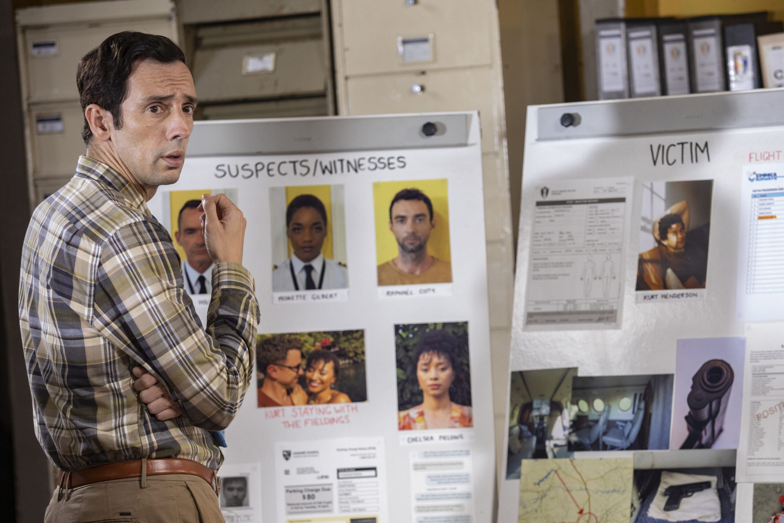 Neville stands before a suspect list in Death in Paradise