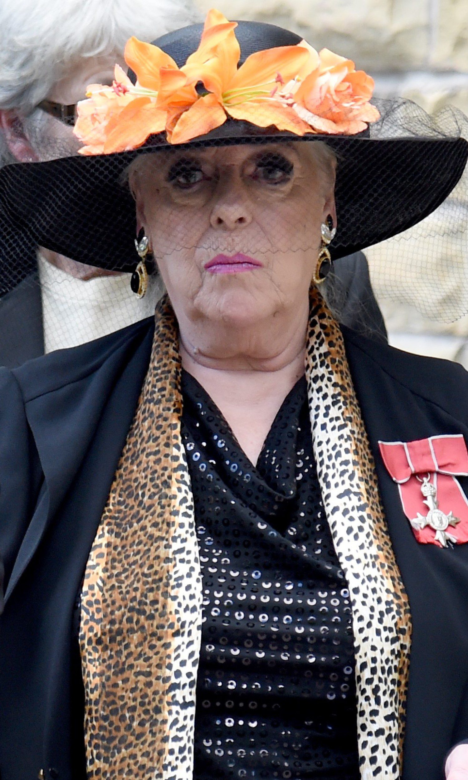 Julie Goodyear looking serious in black outfit and hat