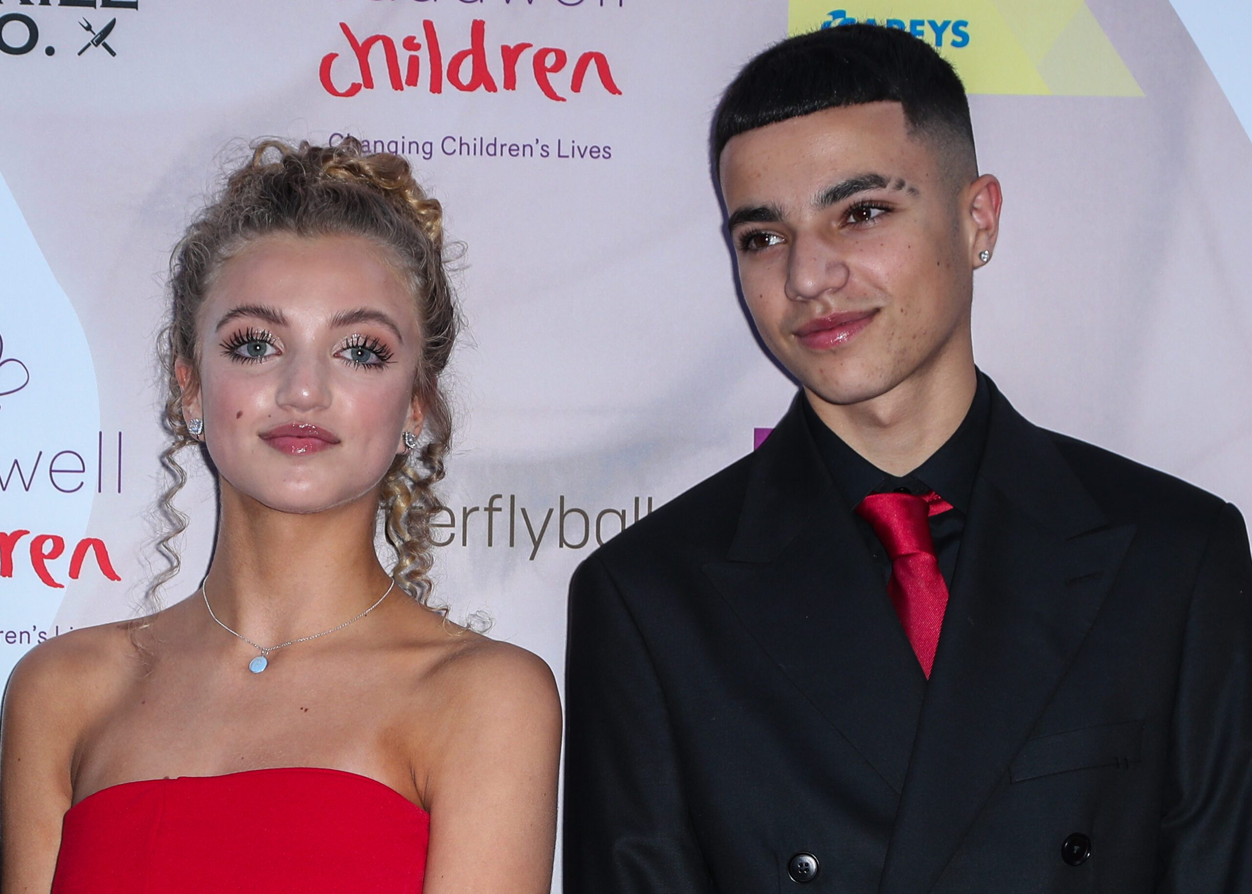 Princess Andre smiling wearing a red dress beside Junior Andre in a black suit with red tie