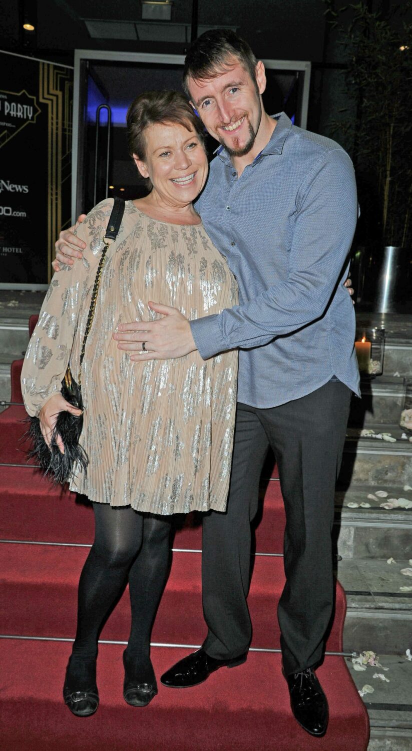Tina Malone and husband Paul Chase smile with his hand on her baby bump