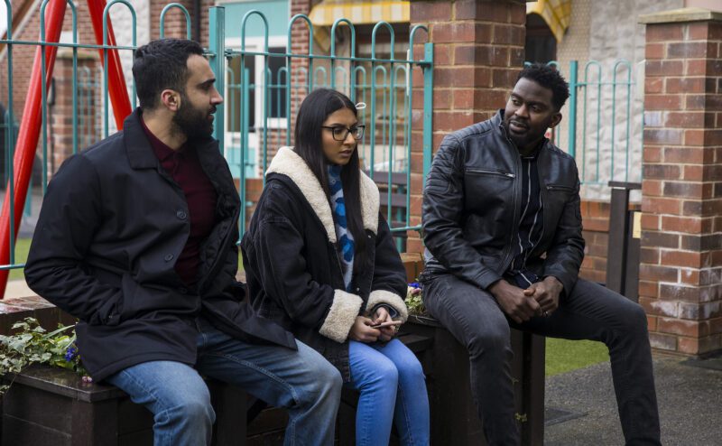 Corrie's Asha looks uncomfortable as two men sit either side of her in the precinct