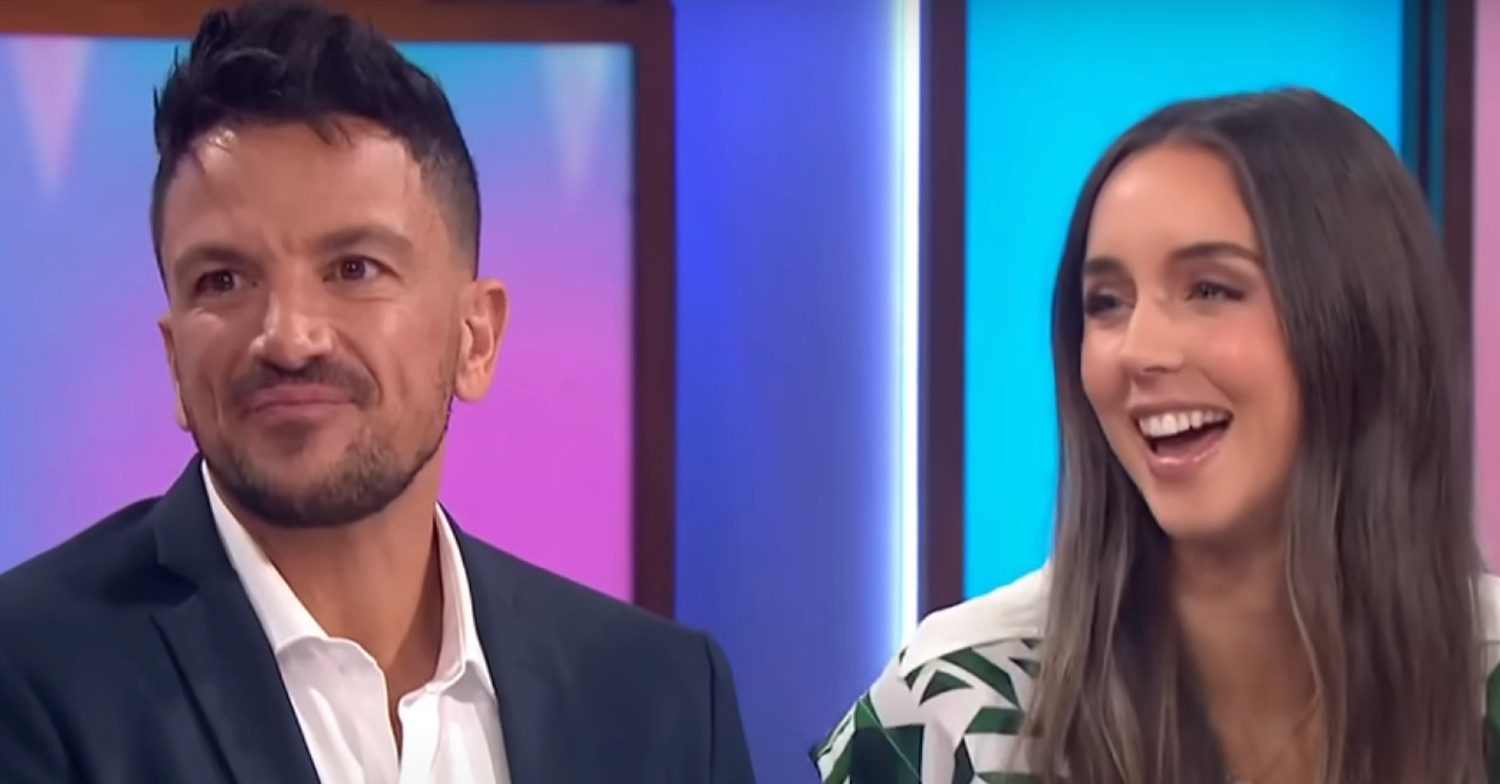 Peter Andre with disgruntled expression beside smiling wife Emily on set of Loose Women