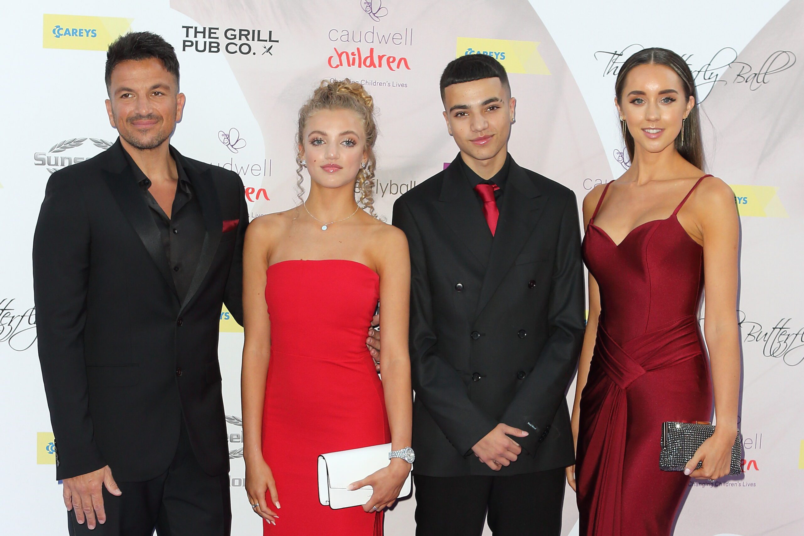 Peter Andre wearing black suit with daughter Princess in red dress, son Junior in black tuxedo and red tie and wife Emily in a red gown