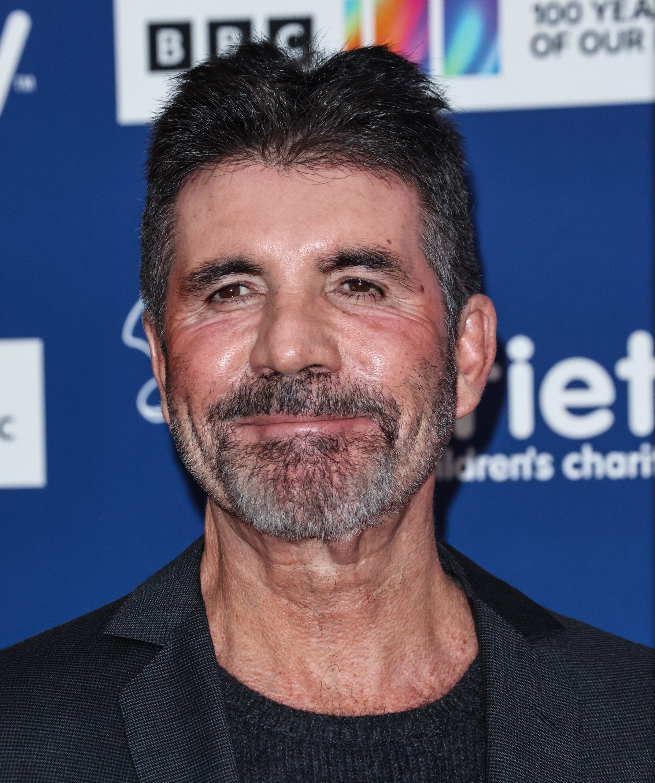 Simon Cowell smiling at camera wearing suit on red carpet