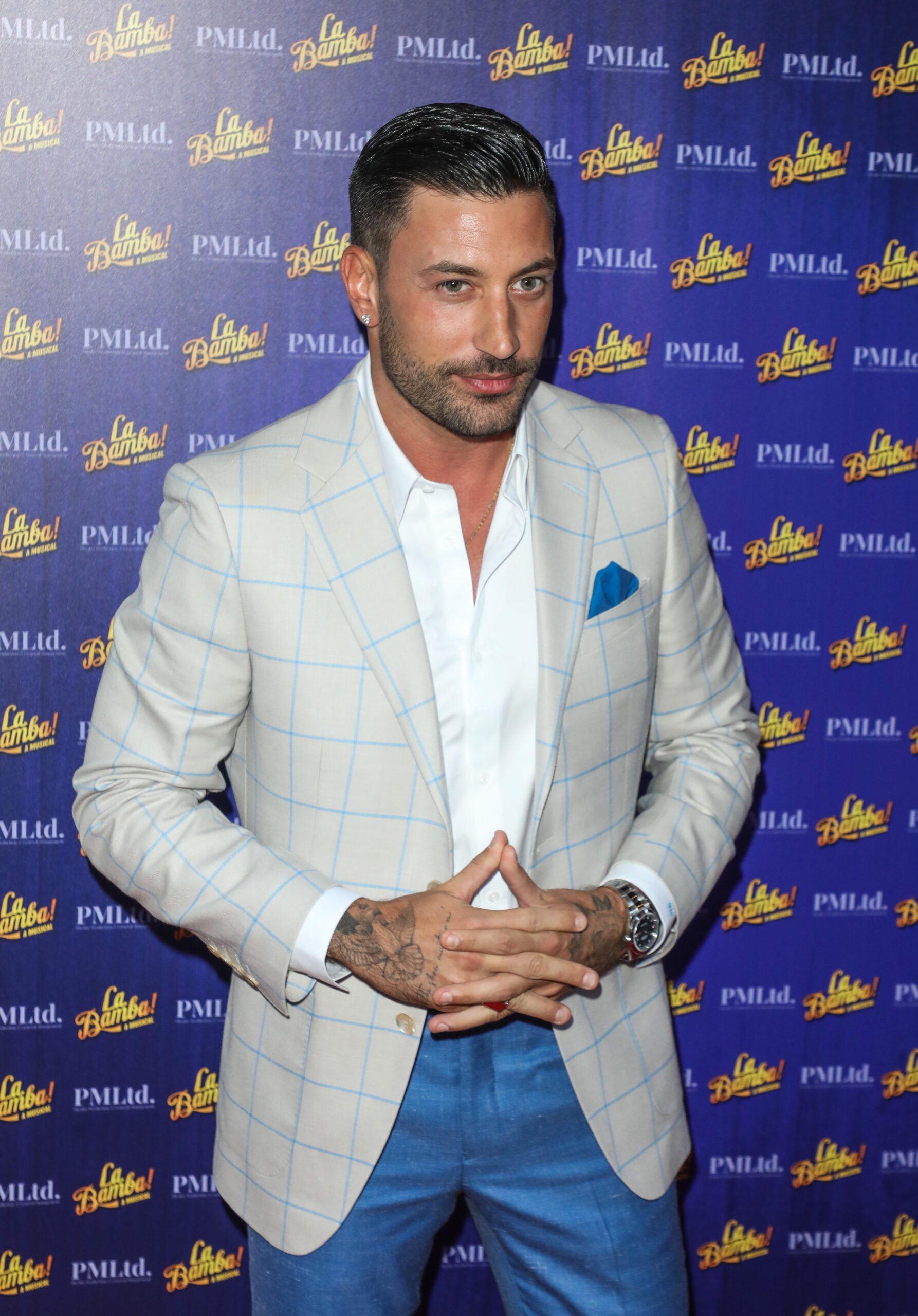 Giovanni Pernice in a grey blazer and white shirt, smiling at a red carpet event