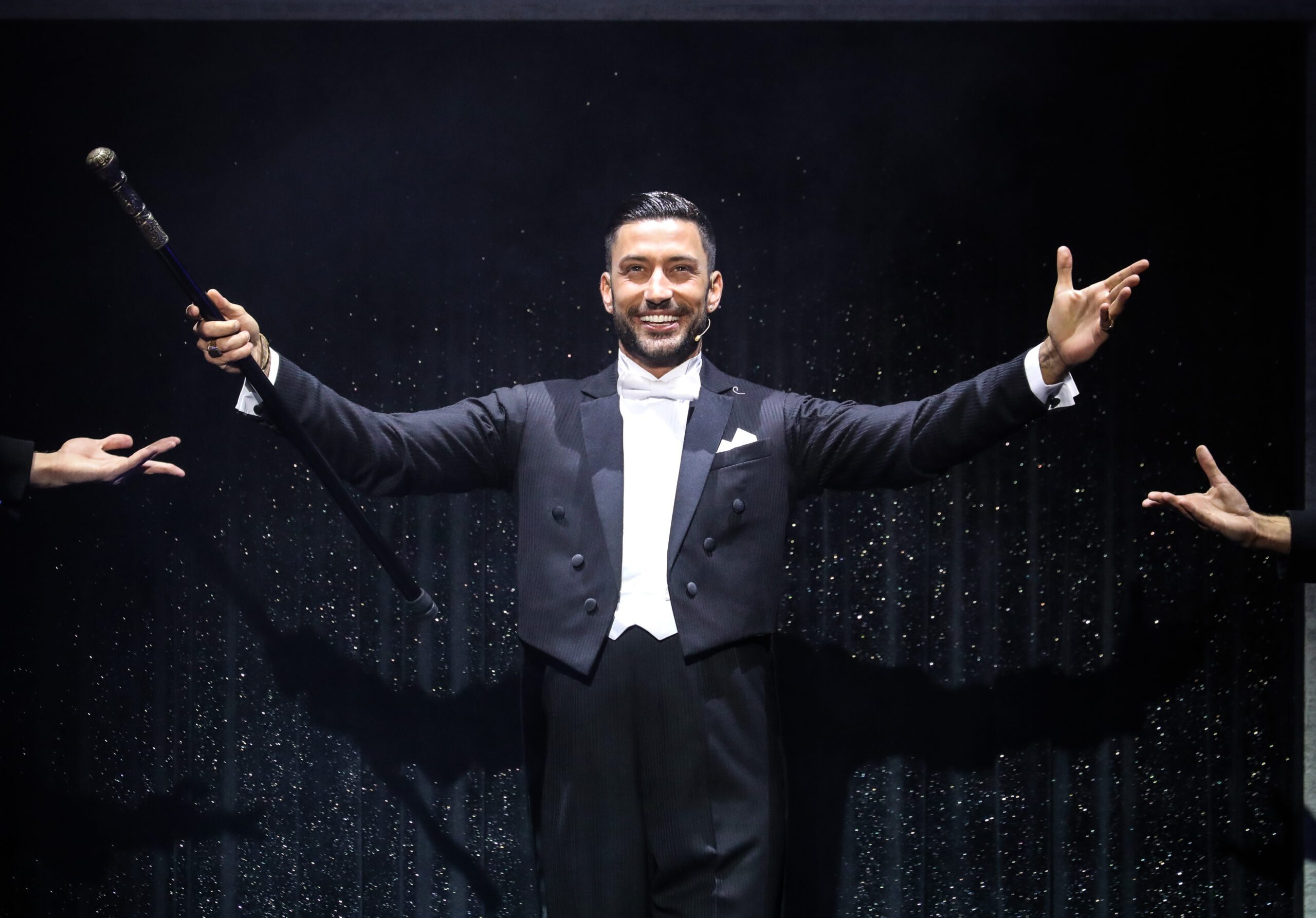 Giovanni Pernice on stage wearing a black tuxedo with outstretched arms