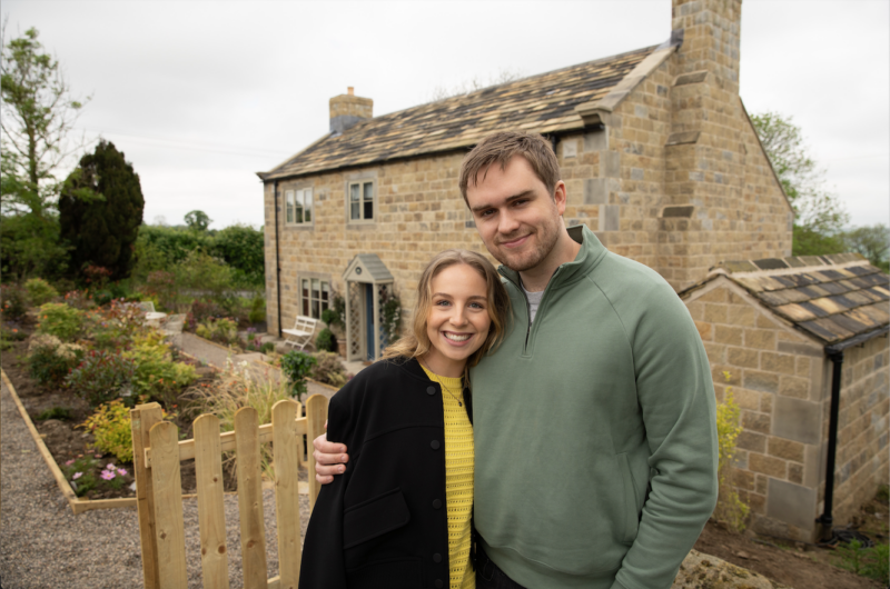 Emmerdale's Belle and Tom are smiling in front of the cottage